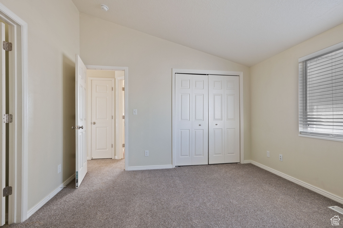 Unfurnished bedroom featuring vaulted ceiling, light colored carpet, and a closet