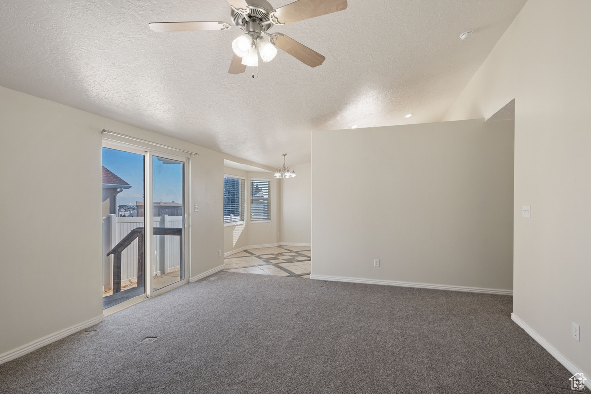 Carpeted empty room with ceiling fan with notable chandelier and a textured ceiling