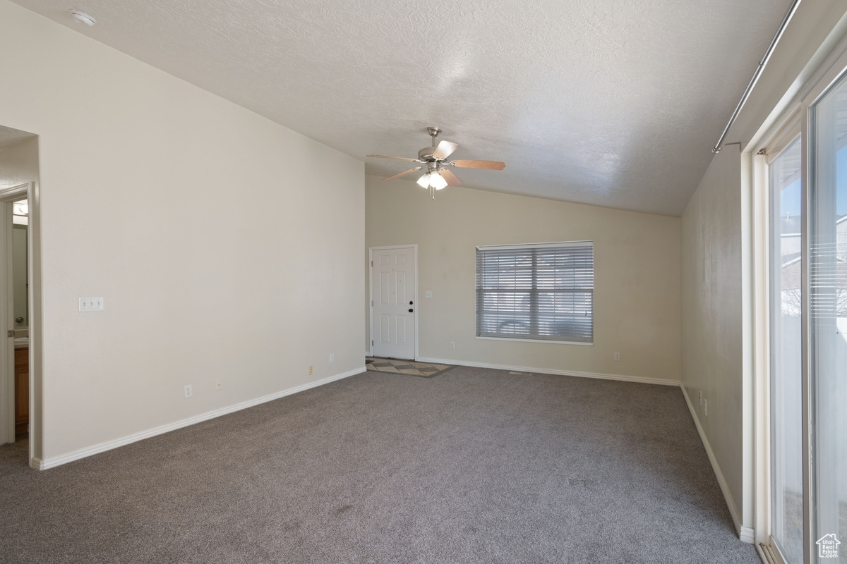 Carpeted empty room with lofted ceiling, ceiling fan, a textured ceiling, and a healthy amount of sunlight