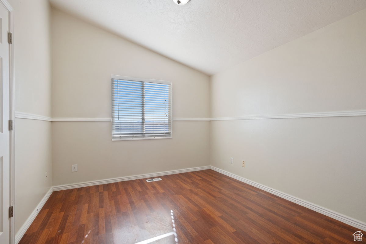 Spare room featuring dark hardwood / wood-style flooring and vaulted ceiling