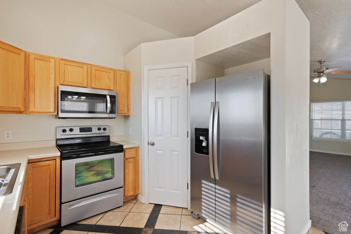 Kitchen featuring light tile patterned floors, a textured ceiling, ceiling fan, and appliances with stainless steel finishes