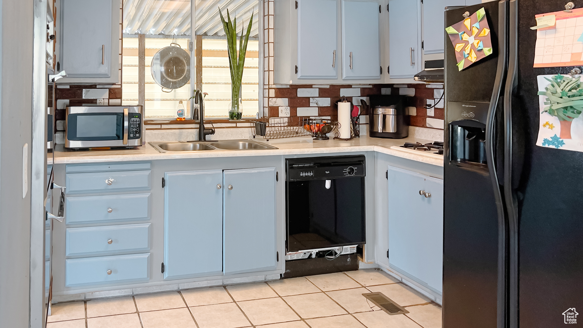 Kitchen featuring tasteful backsplash, light tile patterned floors, sink, and black appliances