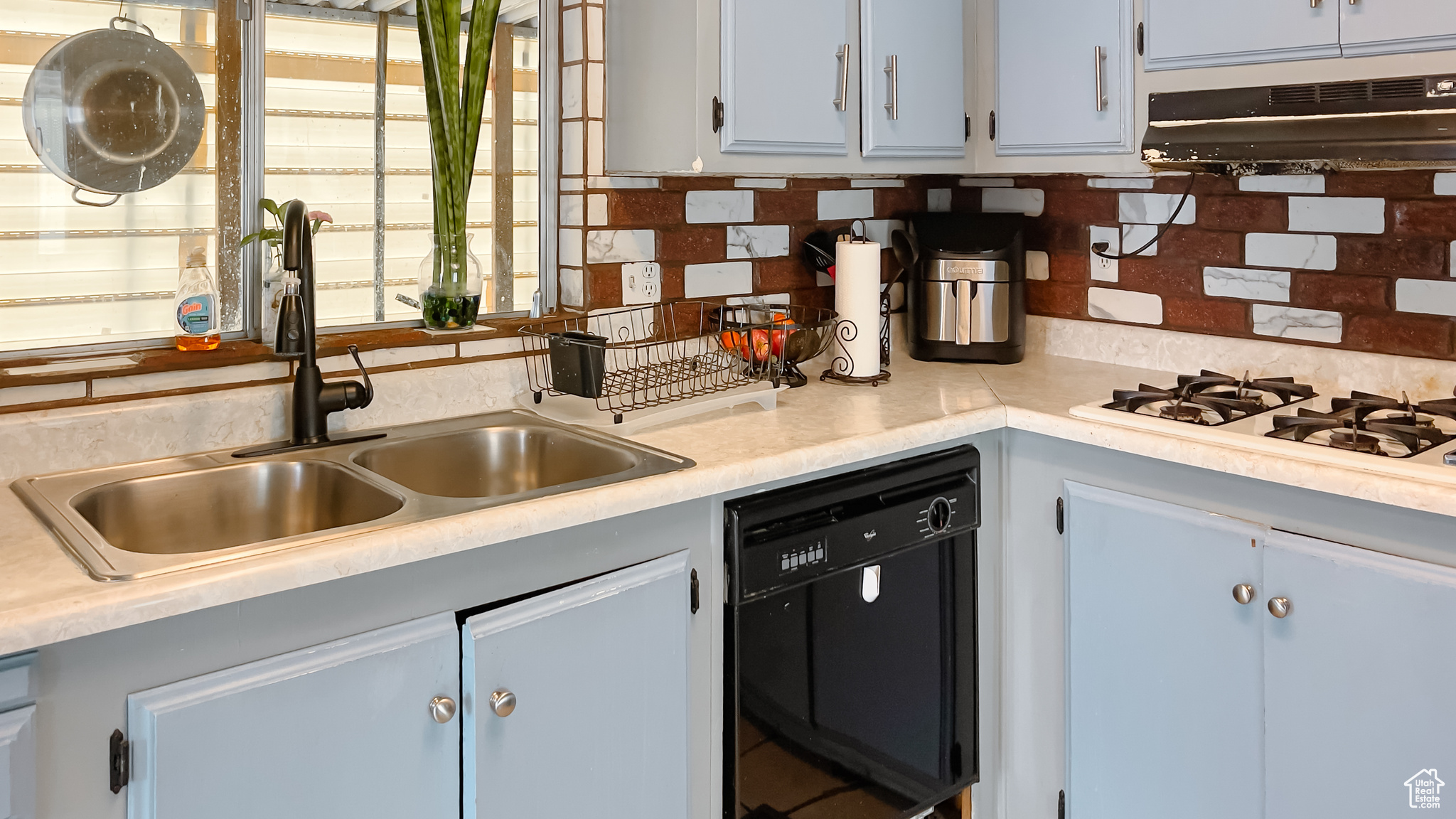 Kitchen with white gas stovetop, tasteful backsplash, black dishwasher, and sink