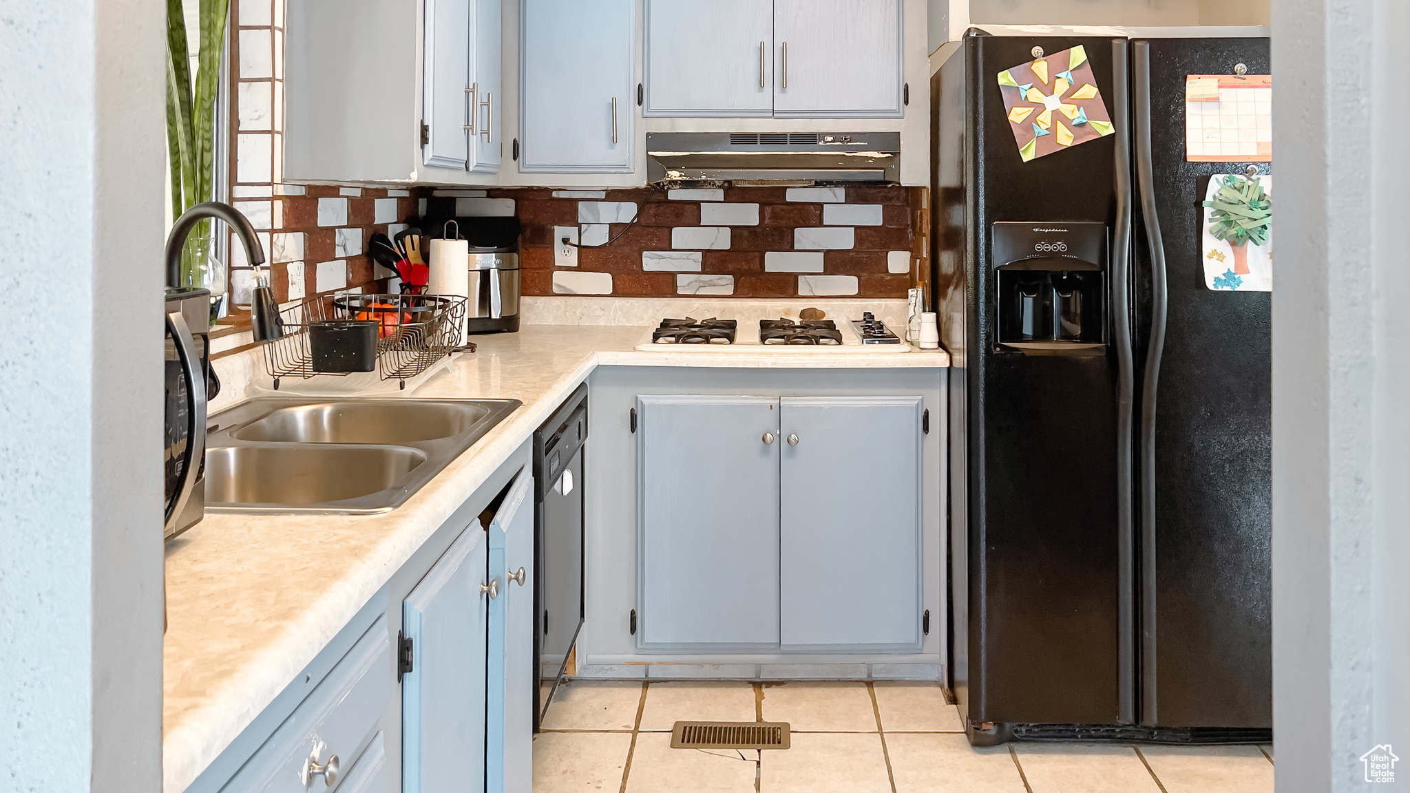 Kitchen featuring sink, light tile patterned floors, black appliances, and decorative backsplash