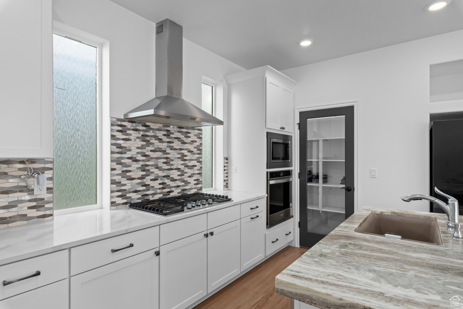 Kitchen featuring sink, appliances with stainless steel finishes, white cabinetry, light stone counters, and wall chimney exhaust hood