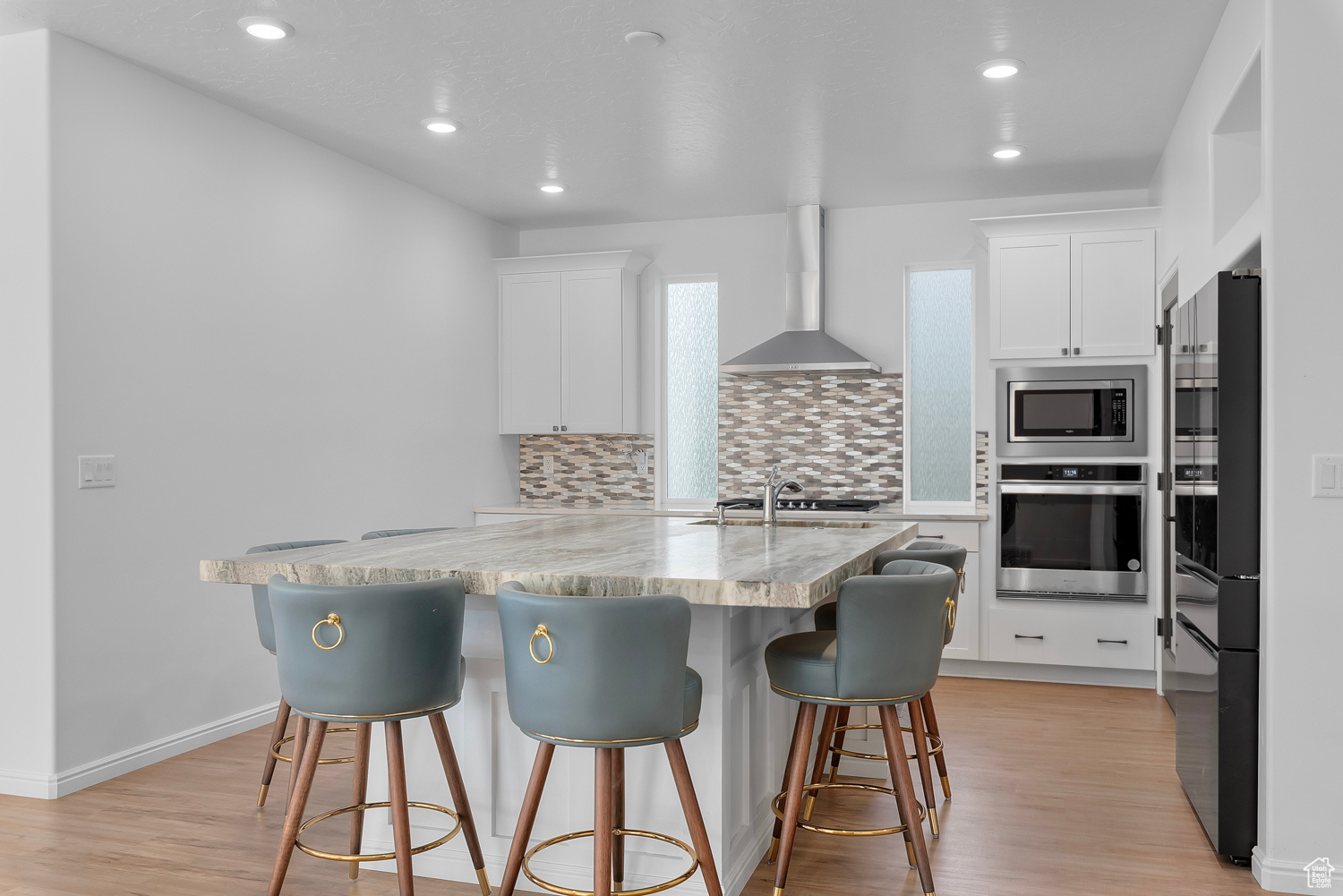 Kitchen featuring white cabinetry, wall chimney range hood, light stone countertops, and appliances with stainless steel finishes