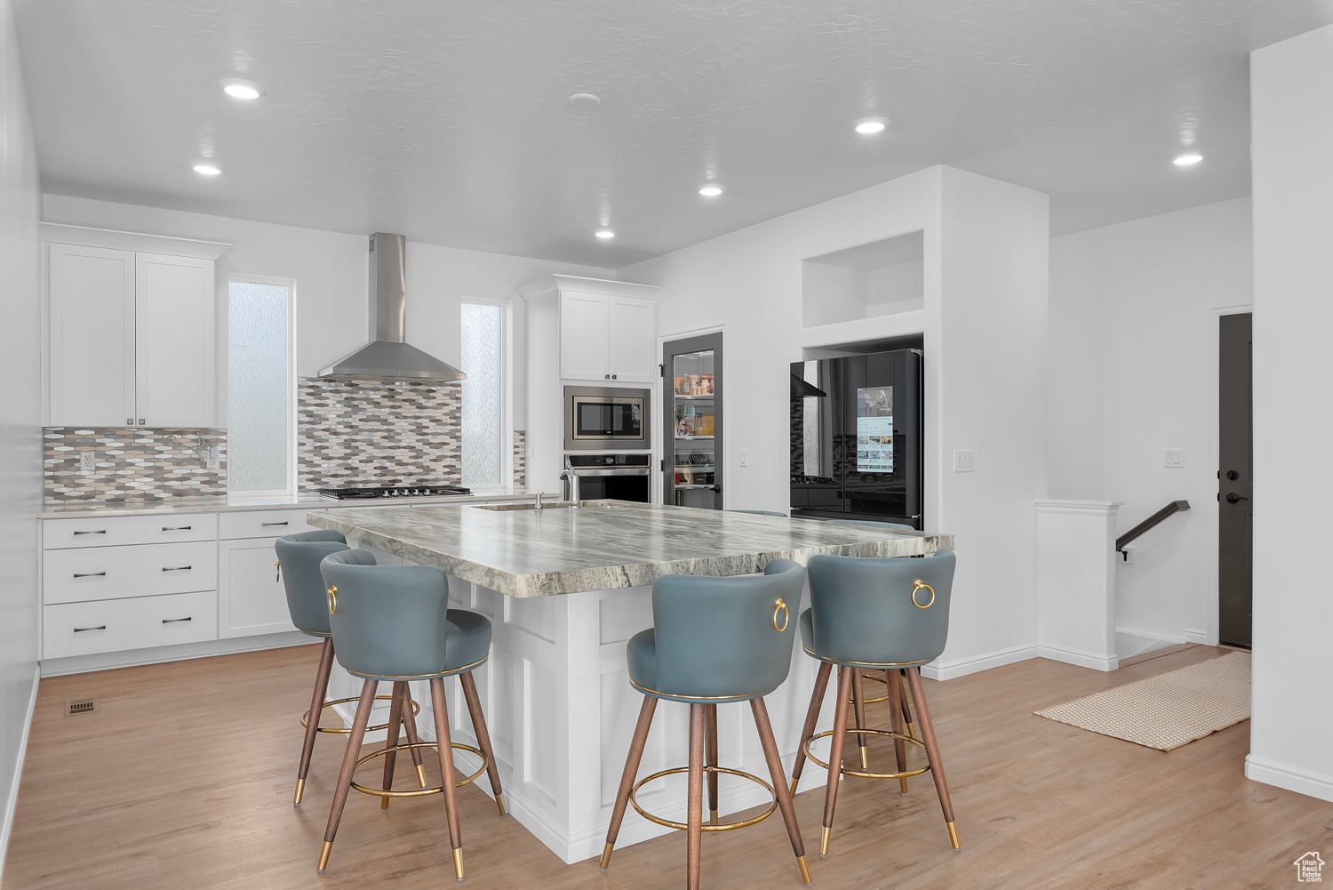 Kitchen featuring appliances with stainless steel finishes, a breakfast bar, white cabinets, a center island with sink, and wall chimney exhaust hood