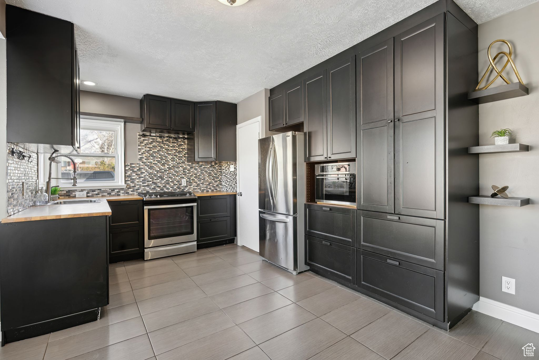 Kitchen featuring sink, a textured ceiling, light tile patterned floors, stainless steel appliances, and decorative backsplash