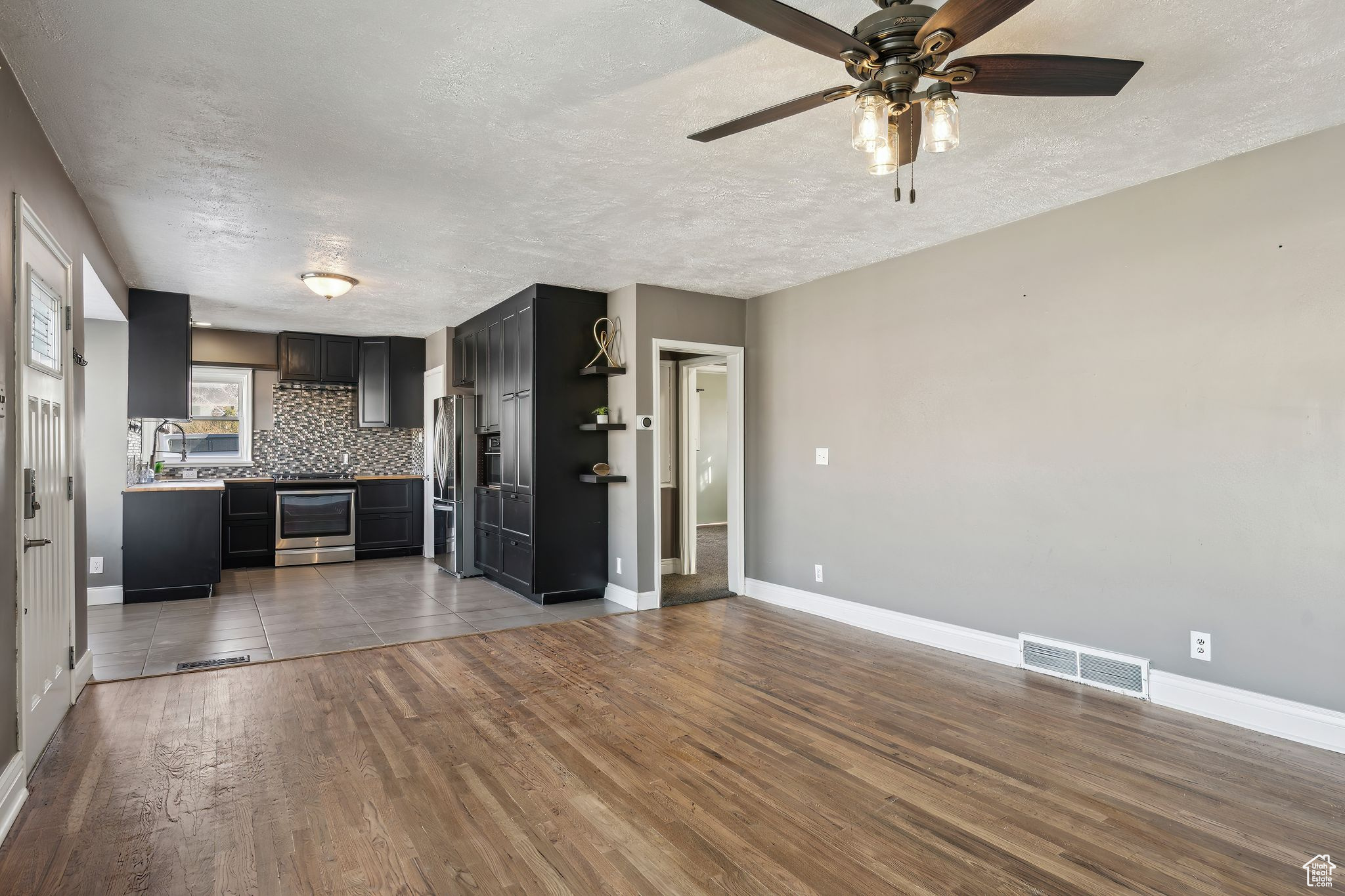 Kitchen featuring stainless steel appliances, tasteful backsplash, a textured ceiling, and light hardwood / wood-style floors