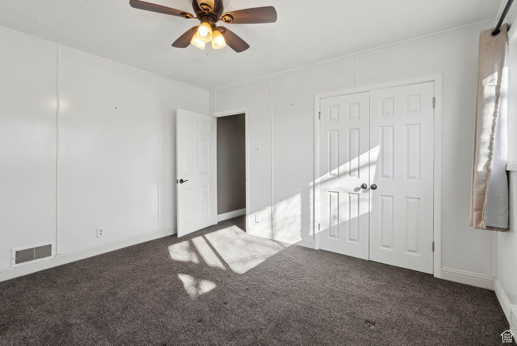 Empty room featuring dark carpet and ceiling fan