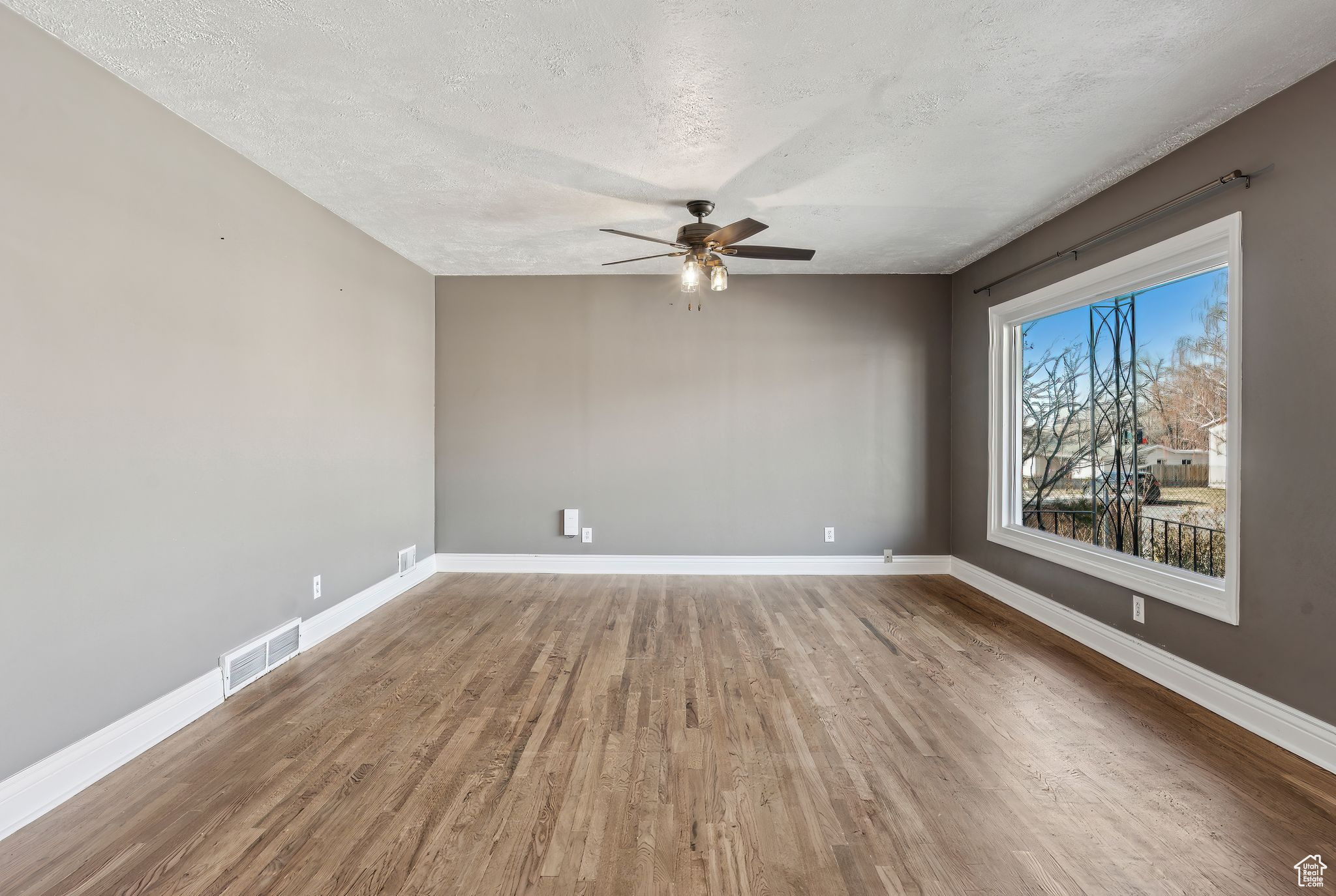 Empty room with ceiling fan, wood-type flooring, and a textured ceiling