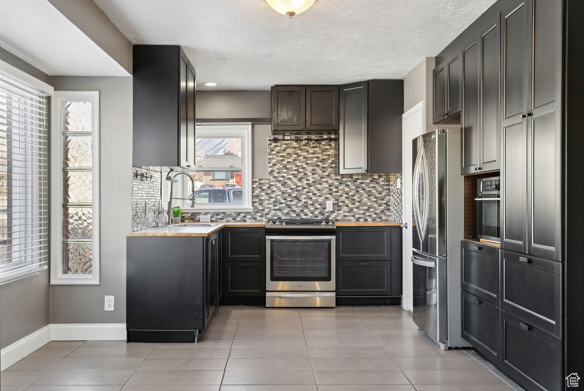 Kitchen with light tile patterned flooring, butcher block countertops, tasteful backsplash, a textured ceiling, and appliances with stainless steel finishes