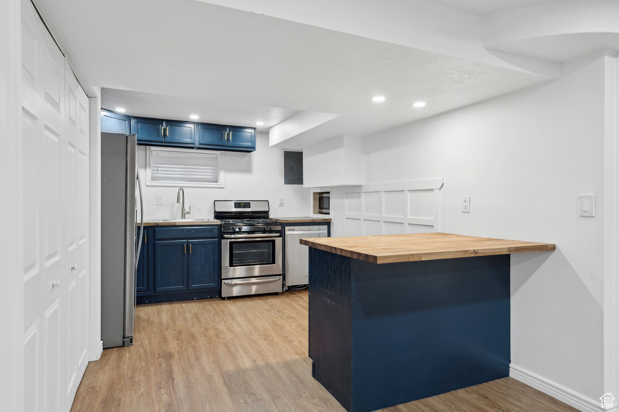 Kitchen with blue cabinets, appliances with stainless steel finishes, wooden counters, and kitchen peninsula