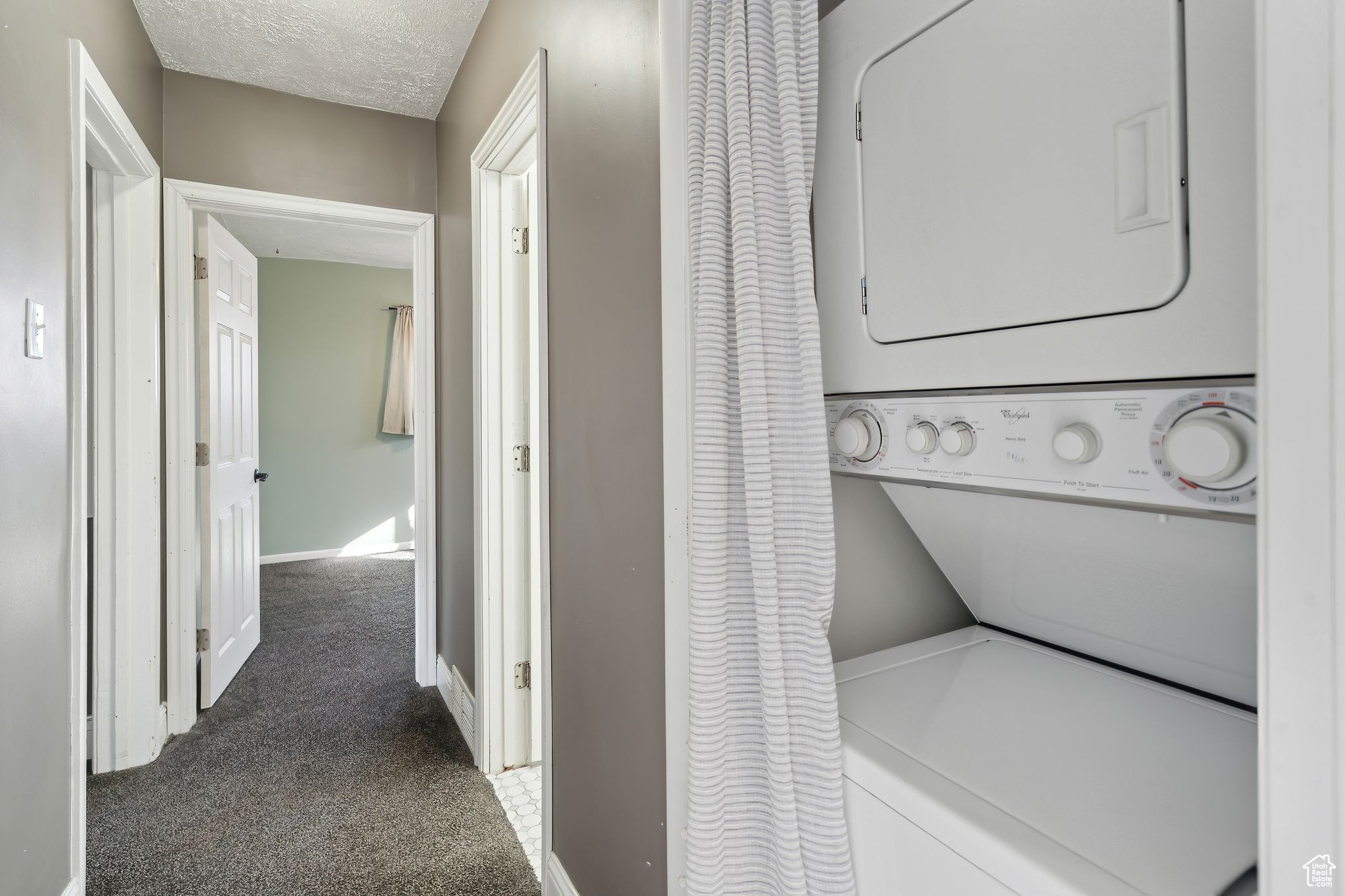 Laundry room featuring dark carpet, a textured ceiling, and stacked washer / dryer