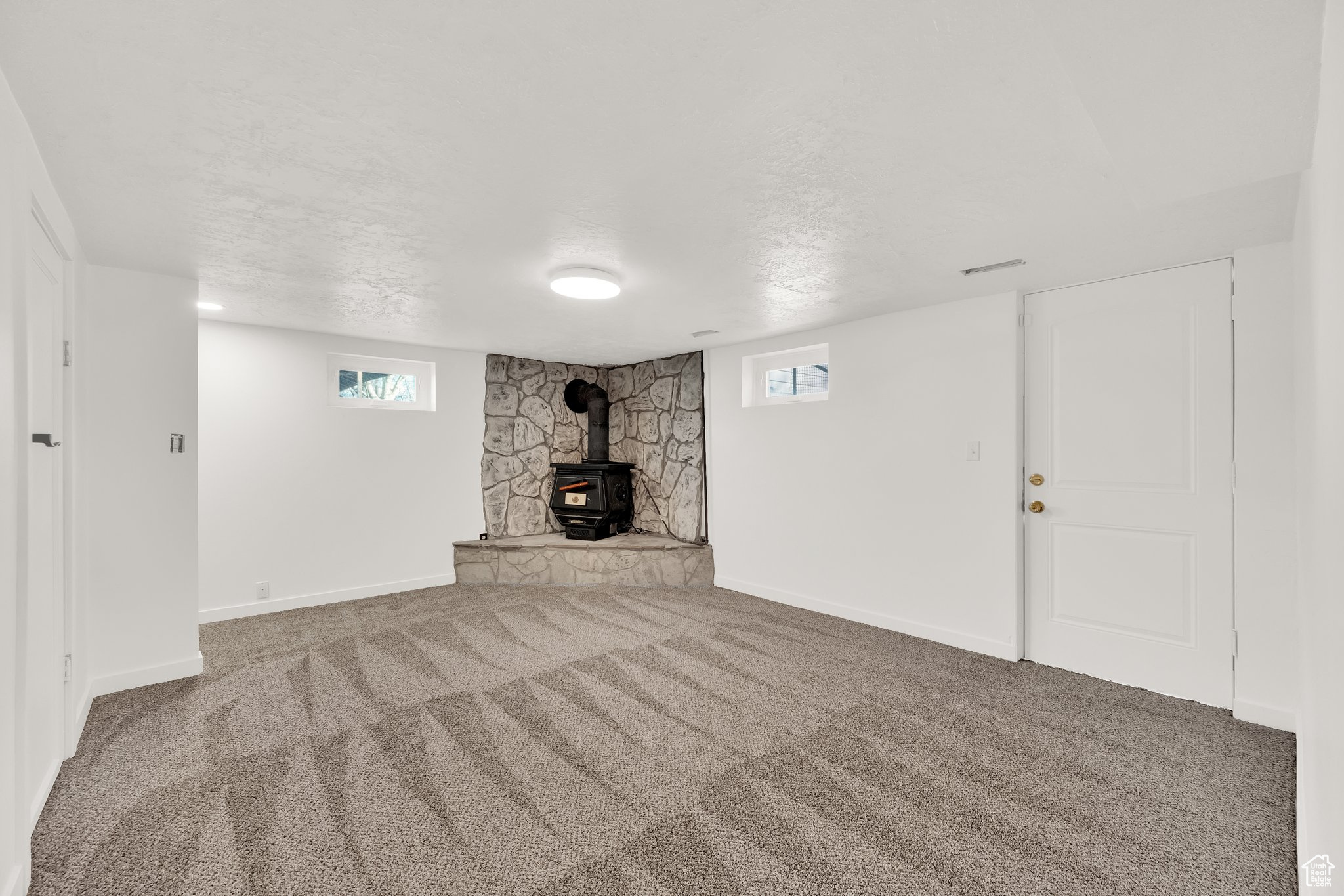 Basement featuring carpet, a wood stove, a textured ceiling, and plenty of natural light