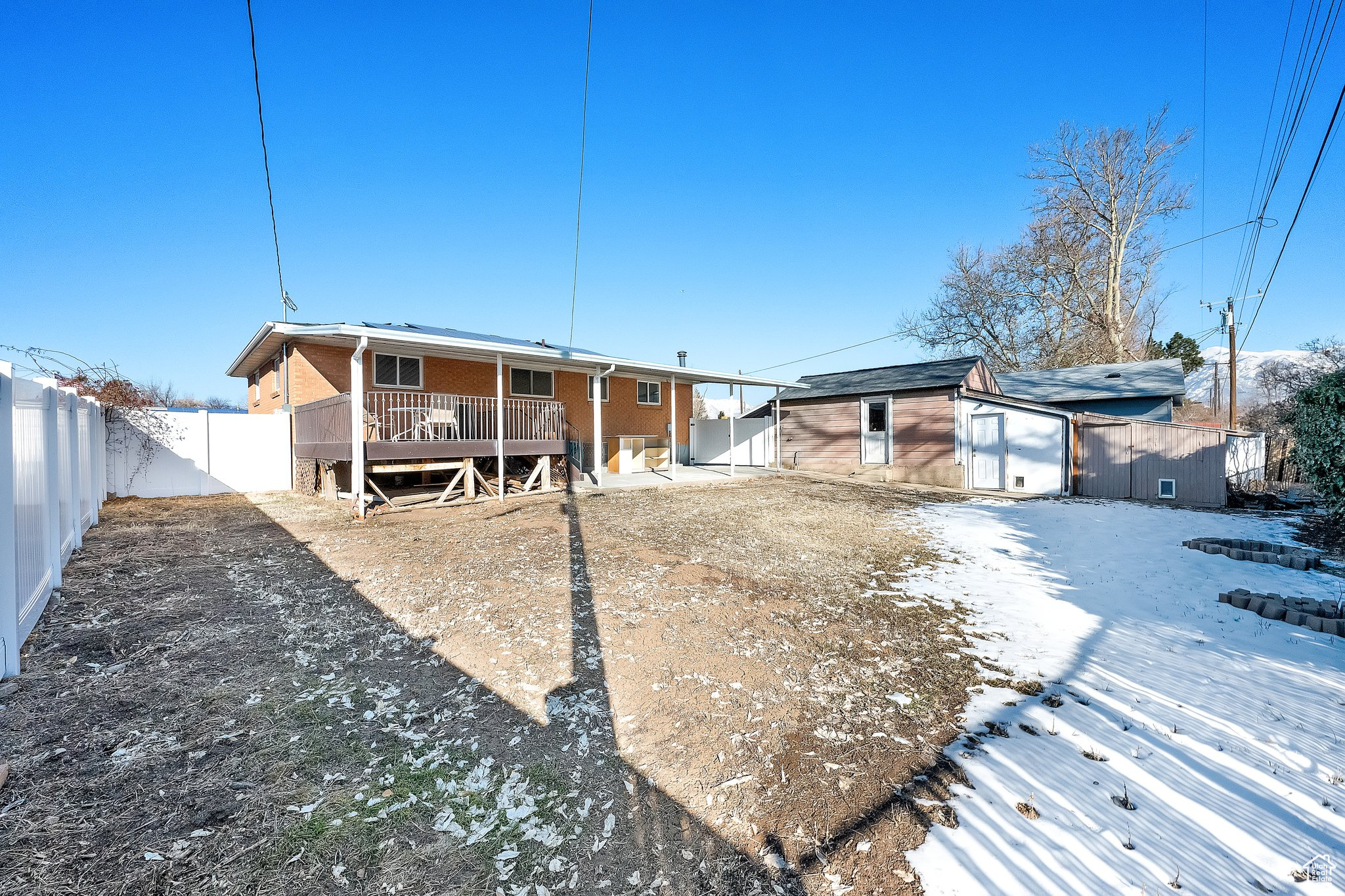 Snow covered back of property with a wooden deck and a storage shed