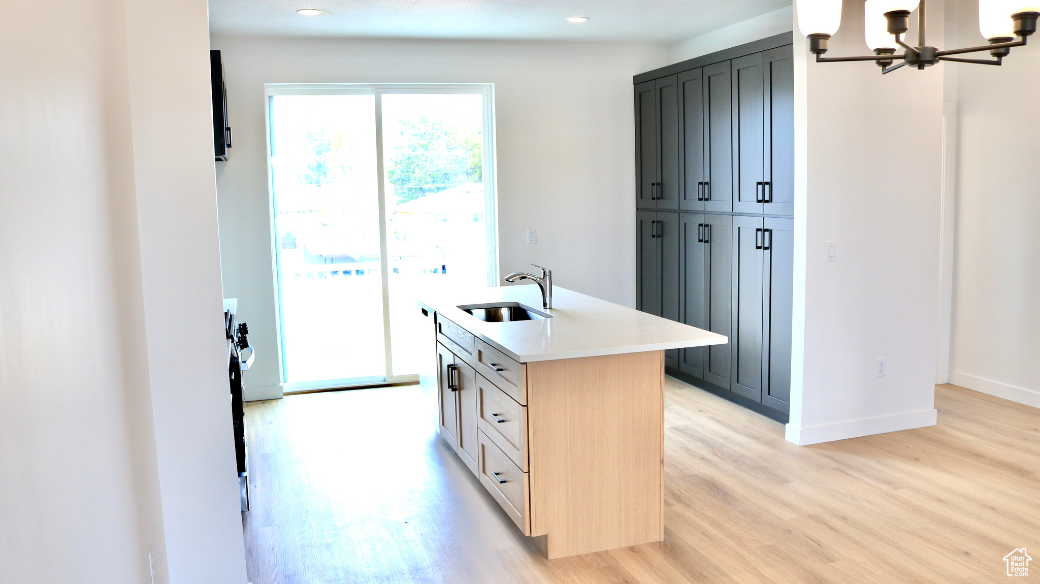 Kitchen with sink, a notable chandelier, light hardwood / wood-style floors, a center island with sink, and light brown cabinets