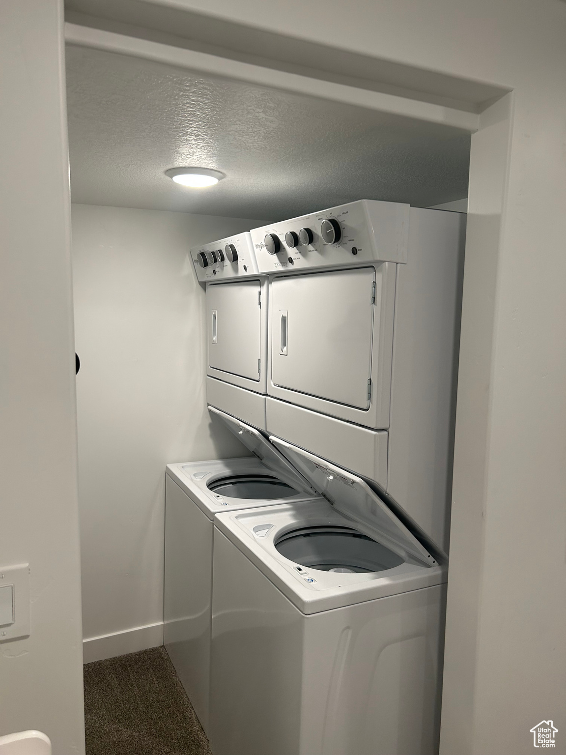 Laundry area with stacked washer and dryer, dark carpet, and a textured ceiling