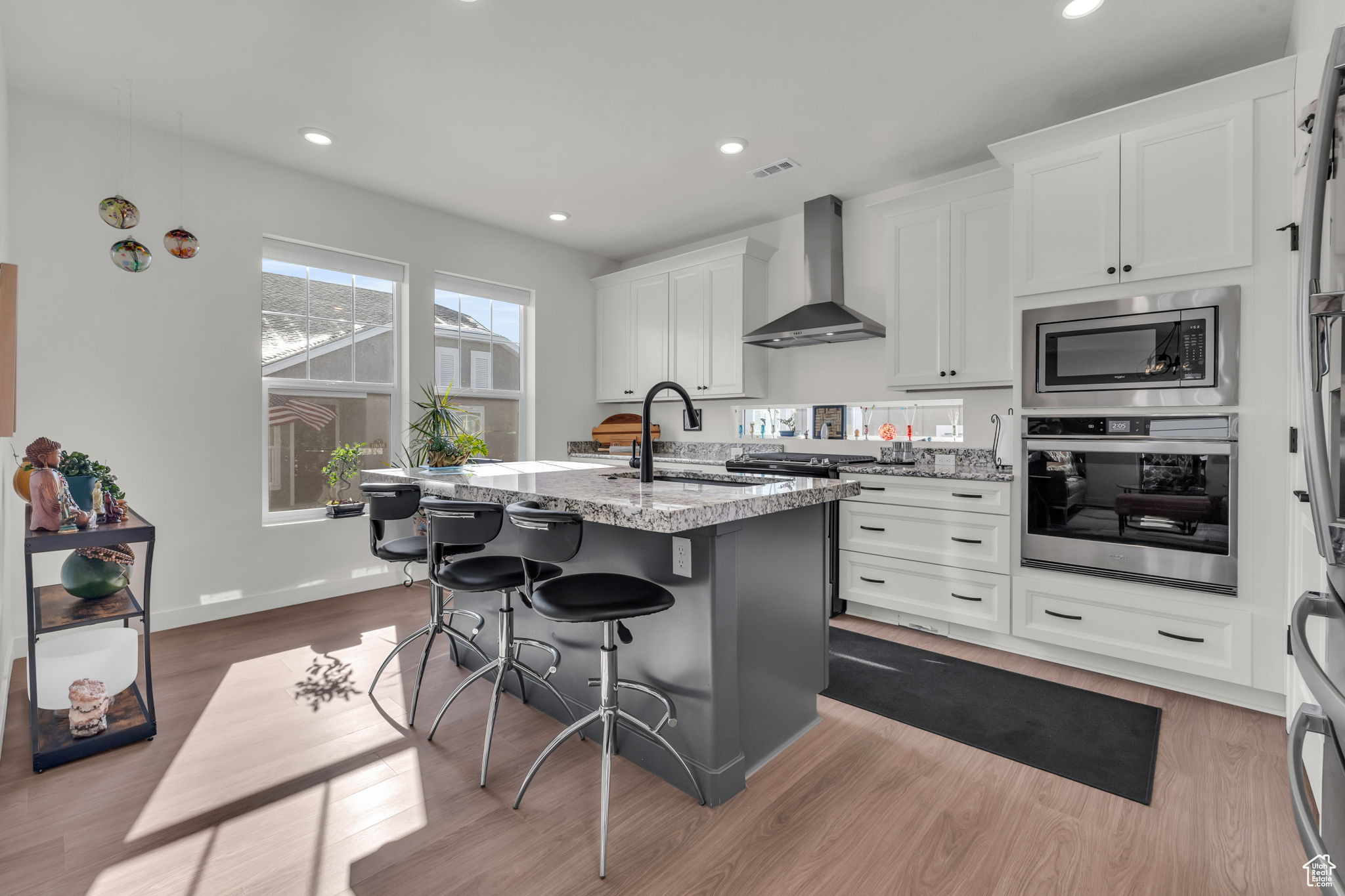 Kitchen with wall chimney range hood, sink, a kitchen island with sink, stainless steel appliances, and a kitchen bar