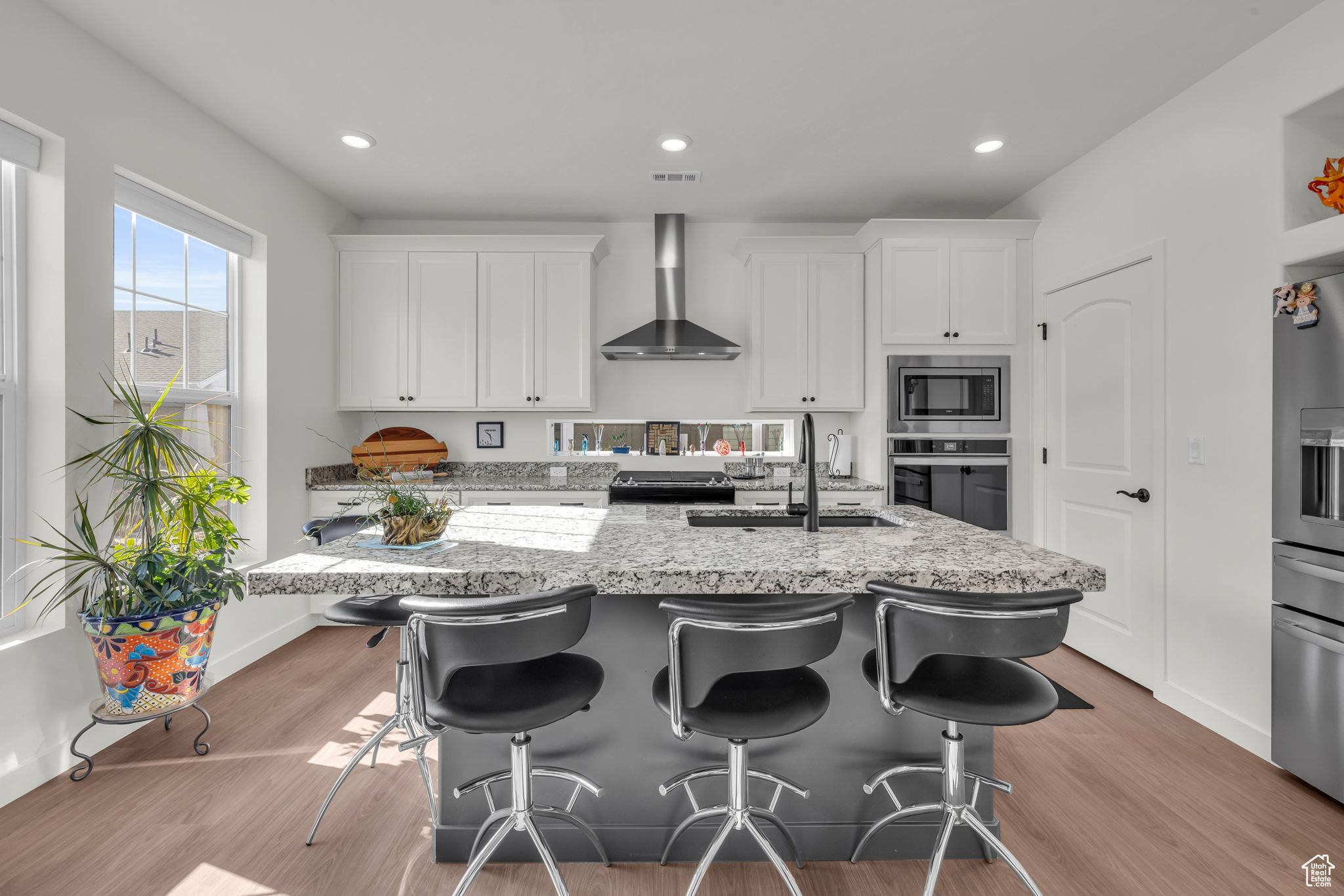 Kitchen with two tone cabinetry, double ovens, gas cooktop, matte black fixtures and island sink