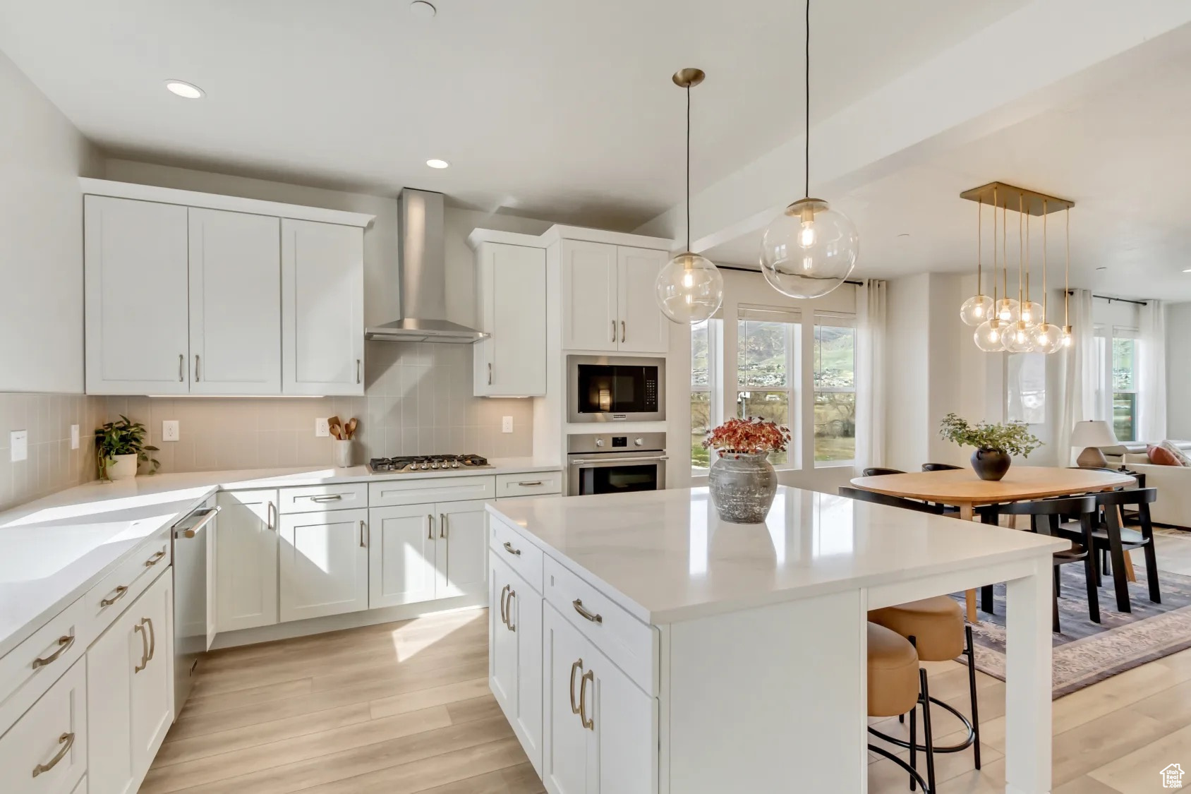 Kitchen featuring white cabinetry, wall chimney range hood, decorative light fixtures, and appliances with stainless steel finishes