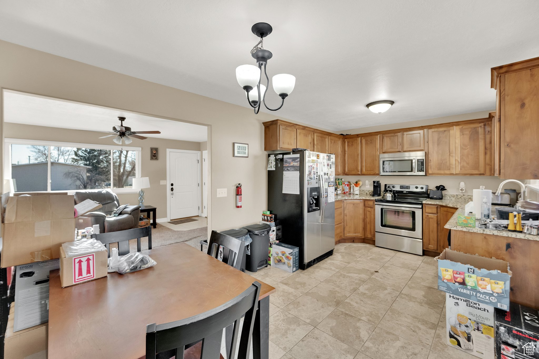 Kitchen with ceiling fan with notable chandelier, decorative light fixtures, sink, light stone counters, and stainless steel appliances