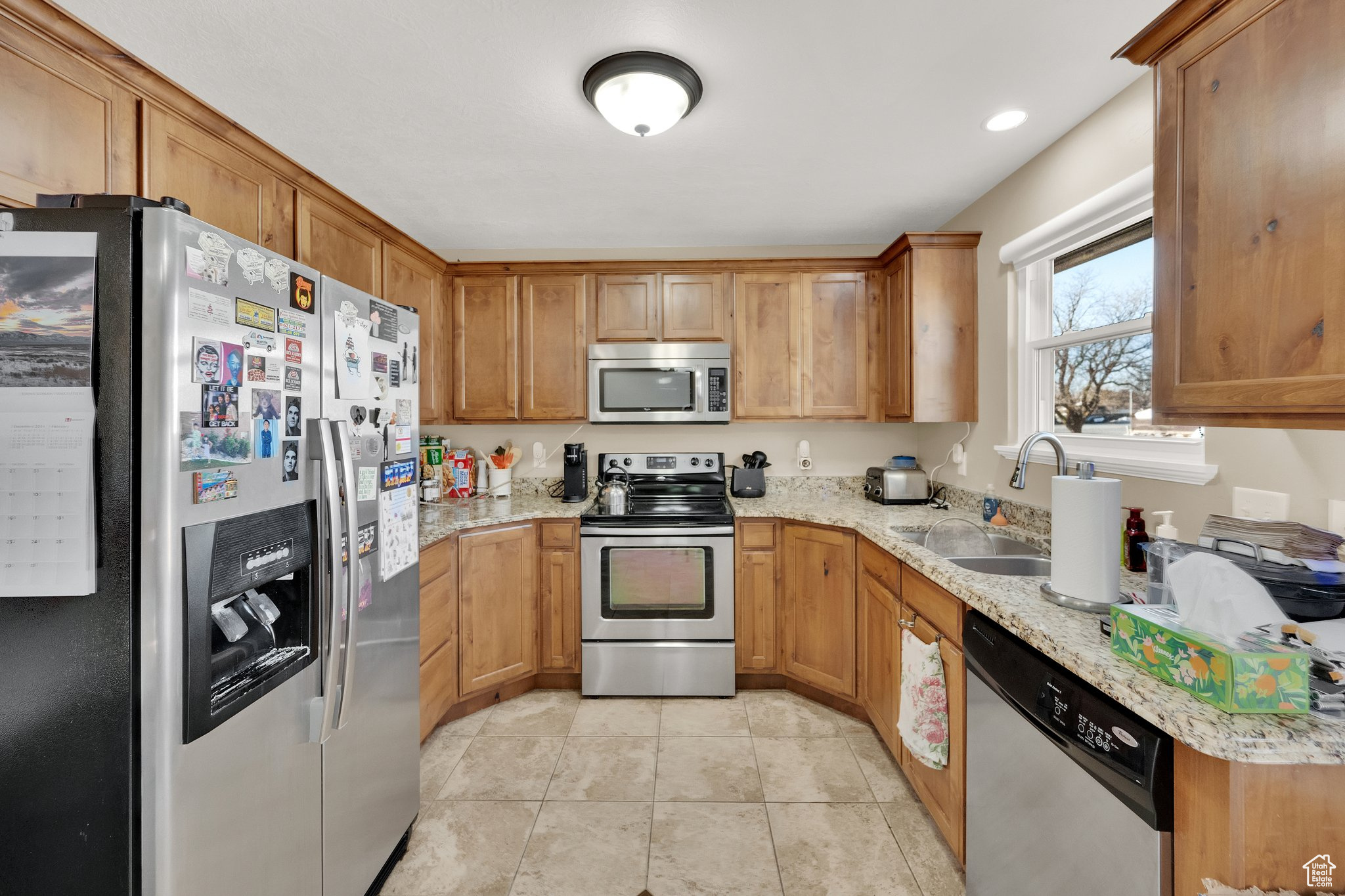 Kitchen with appliances with stainless steel finishes, light stone countertops, sink, and light tile patterned floors