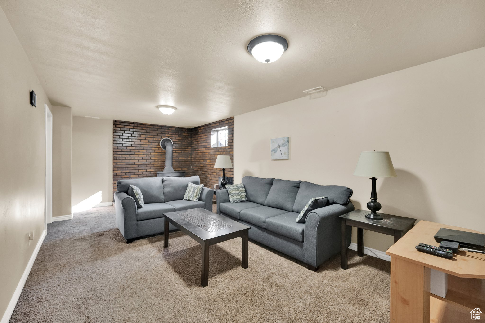 Living room with brick wall, light colored carpet, a textured ceiling, and a wood stove