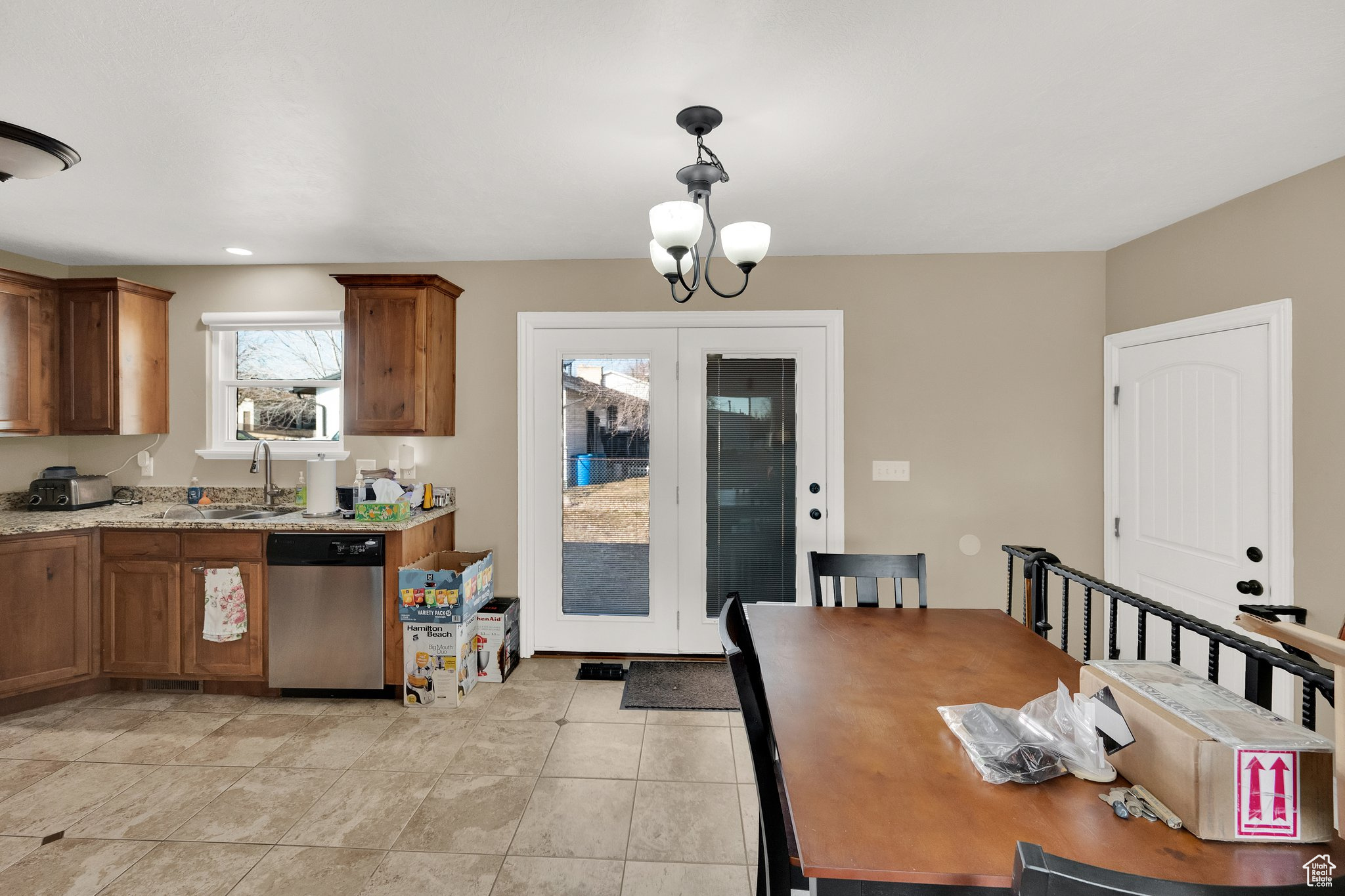 Kitchen with decorative light fixtures, sink, a chandelier, stainless steel dishwasher, and light stone counters