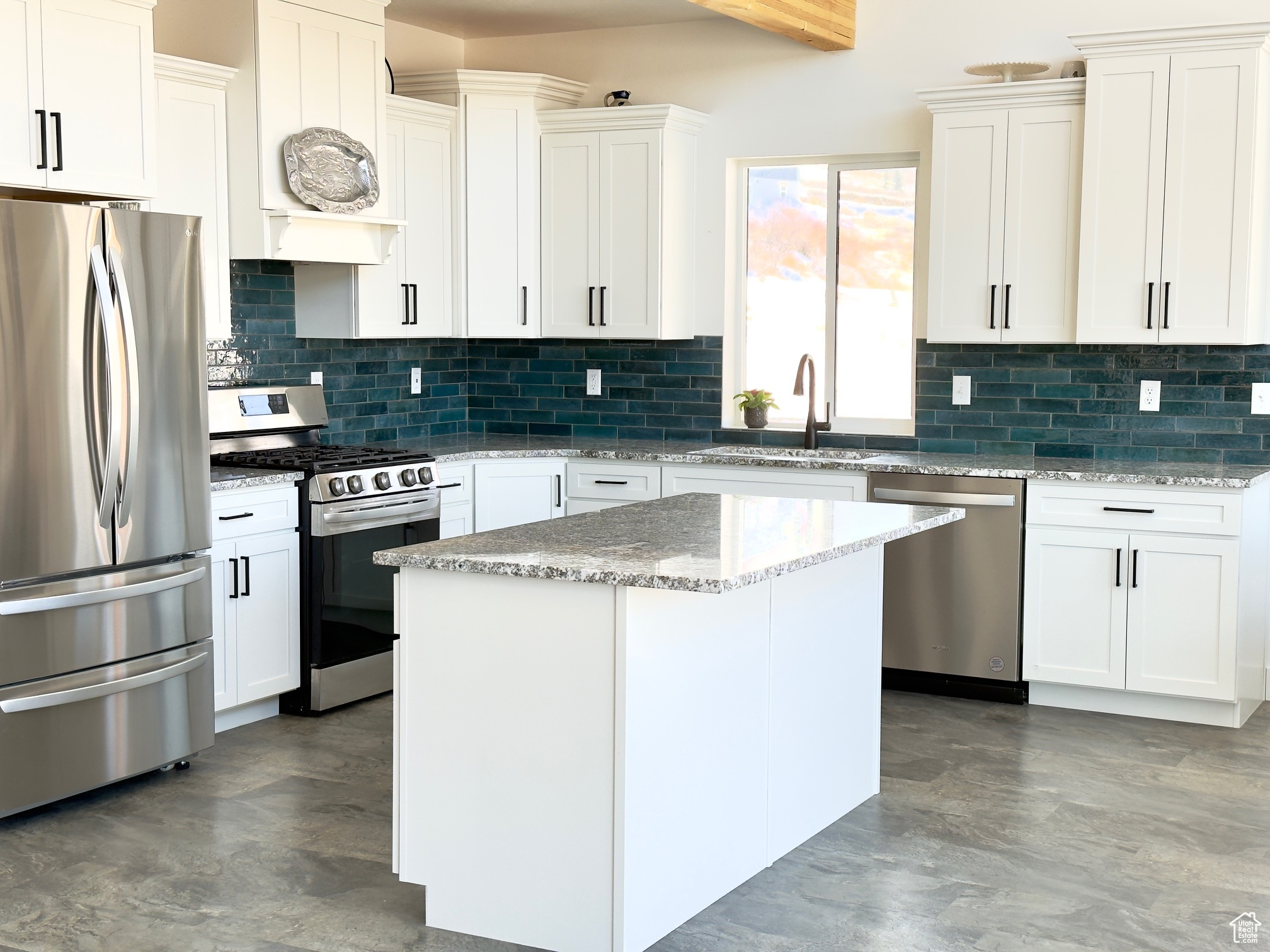 Kitchen with appliances with stainless steel finishes, sink, white cabinets, a center island, and light stone countertops