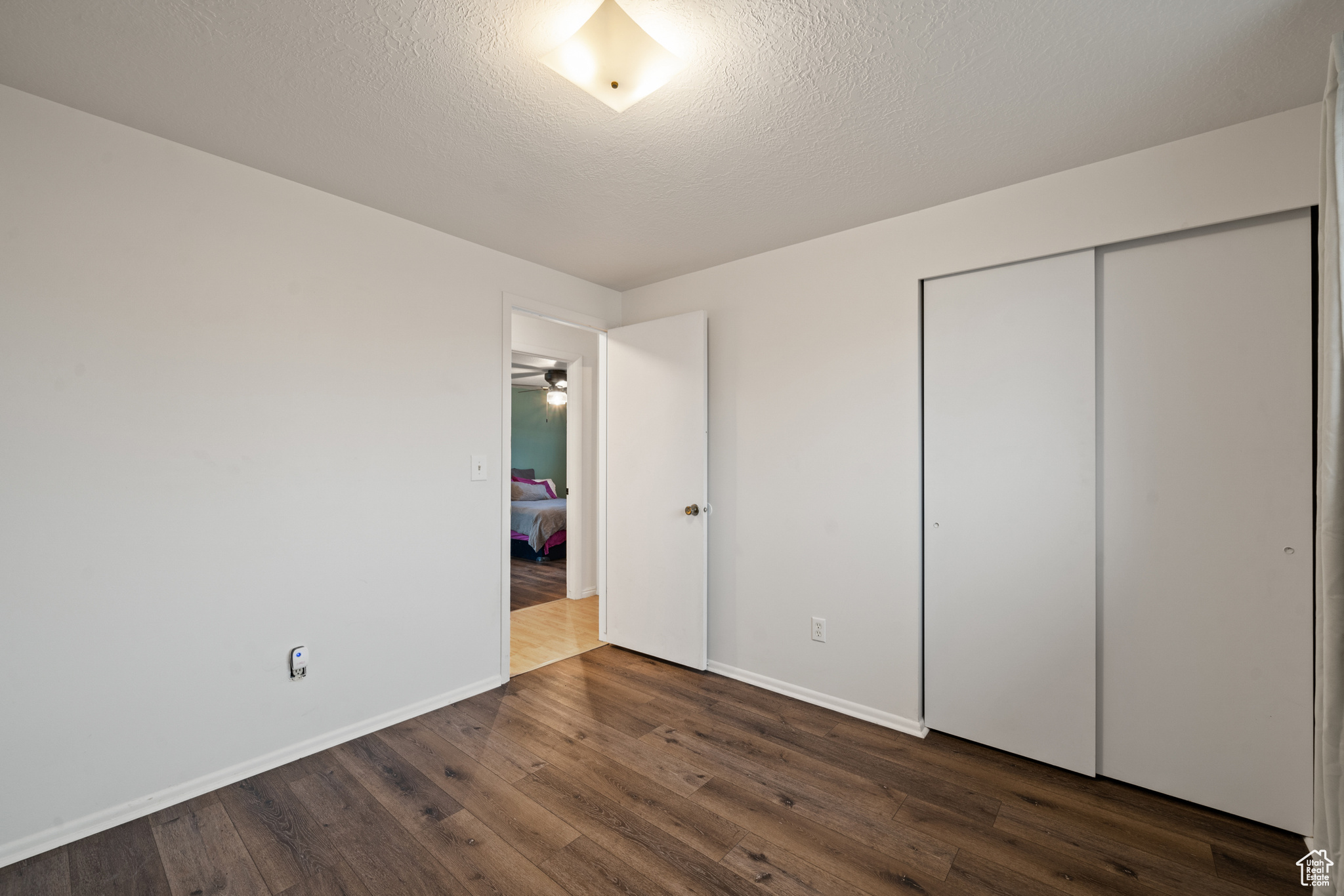 Unfurnished bedroom featuring dark hardwood / wood-style floors, a textured ceiling, and a closet