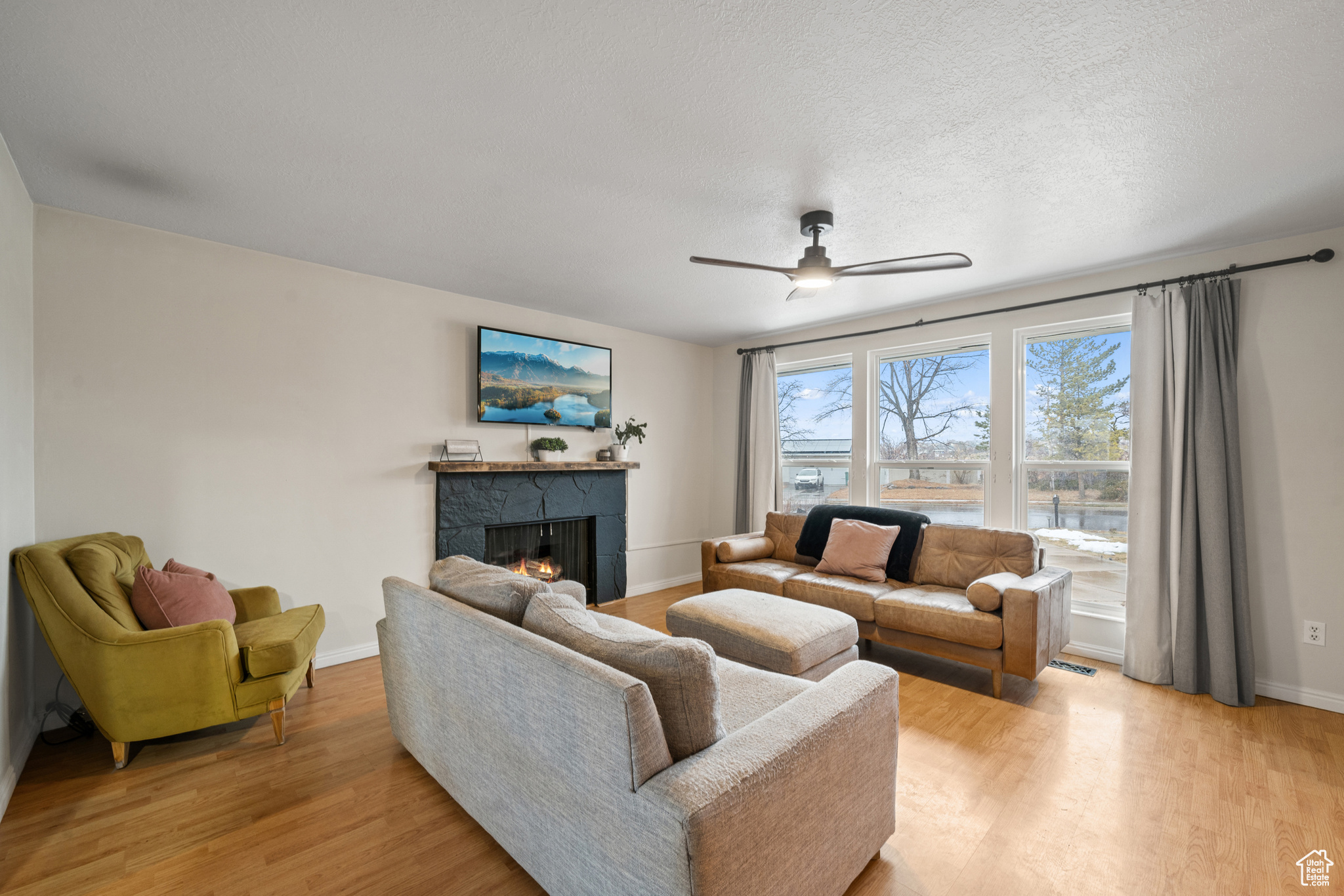 Living room featuring ceiling fan, a tile fireplace, light hardwood / wood-style flooring, and a textured ceiling