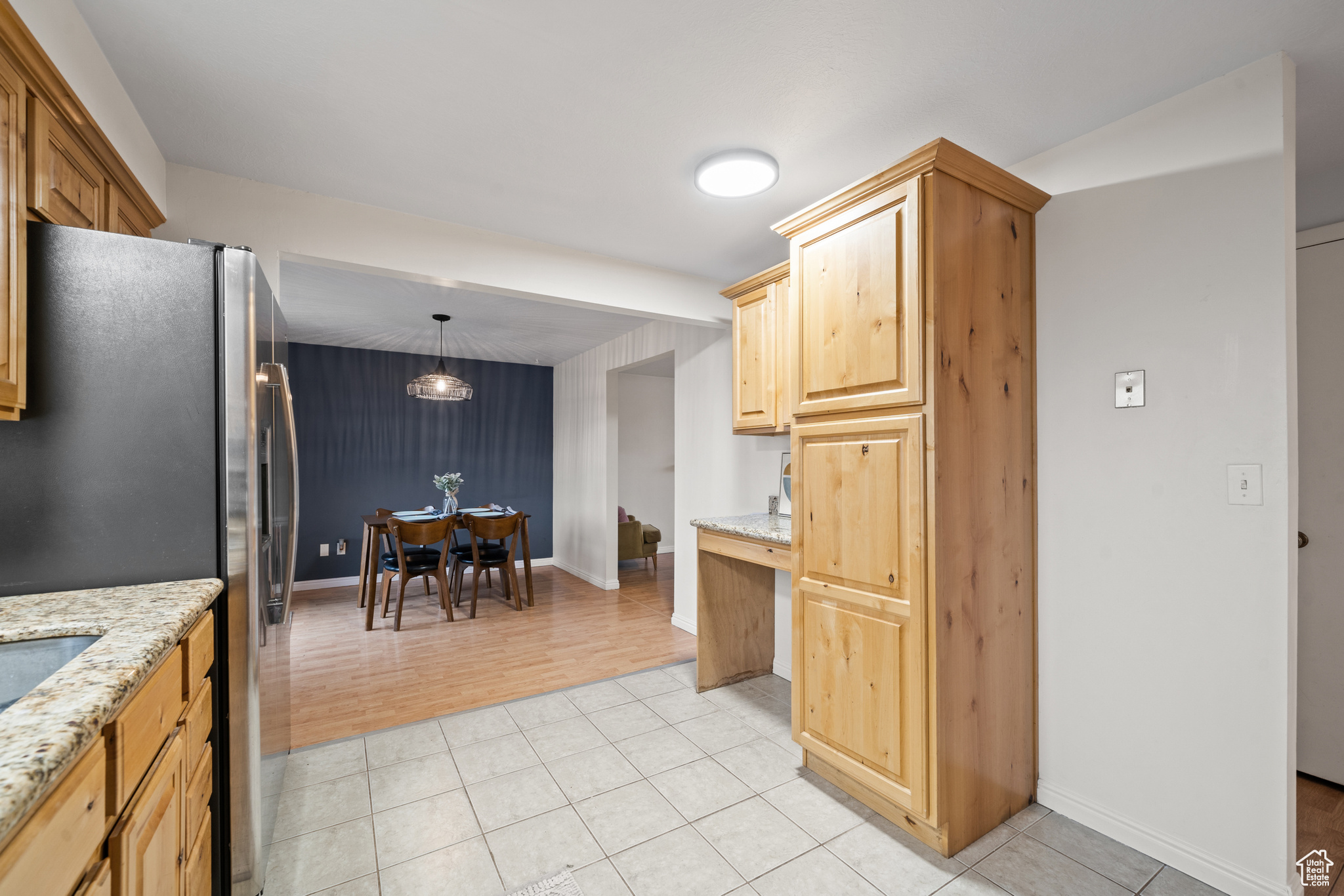 Kitchen featuring pendant lighting, light tile patterned floors, light stone countertops, and stainless steel refrigerator