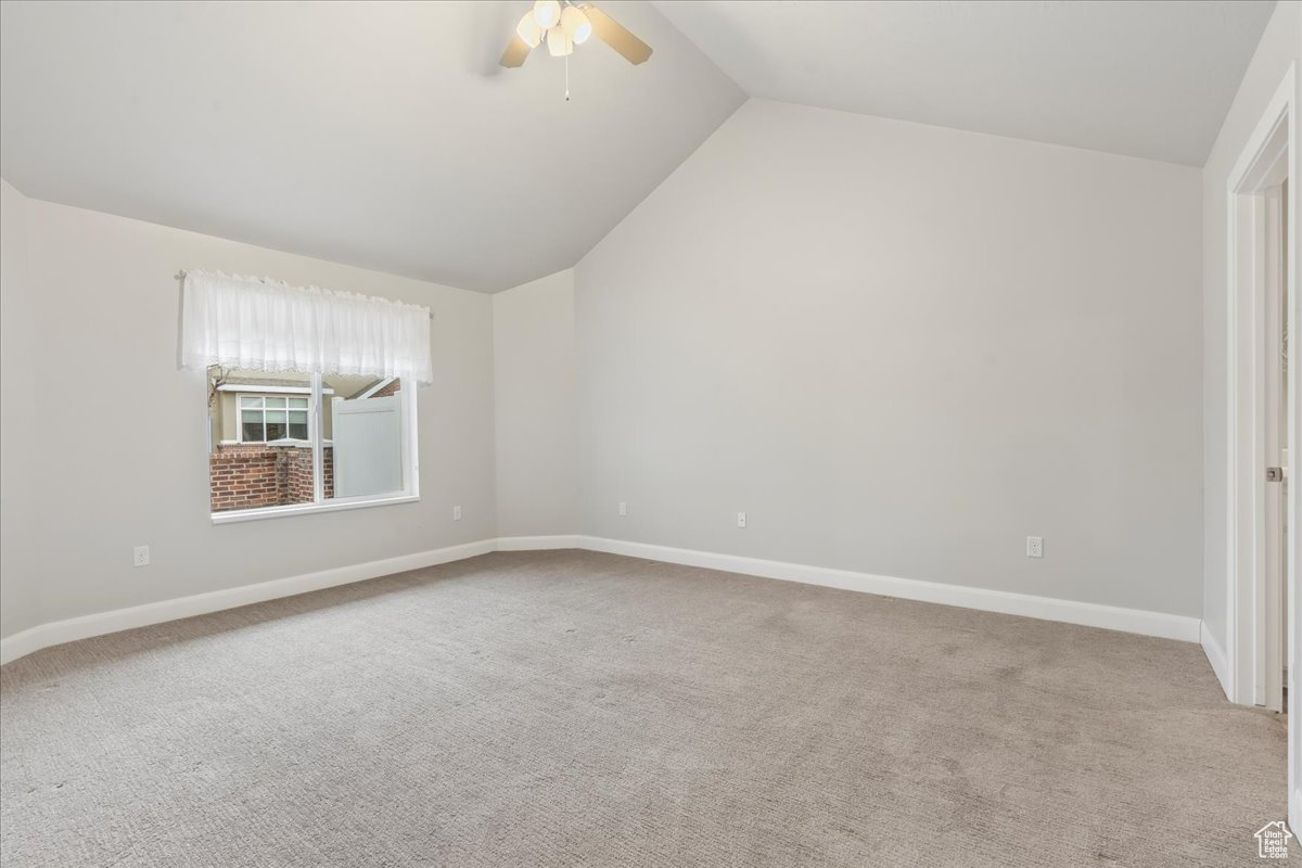 Empty room featuring ceiling fan, lofted ceiling, and light carpet