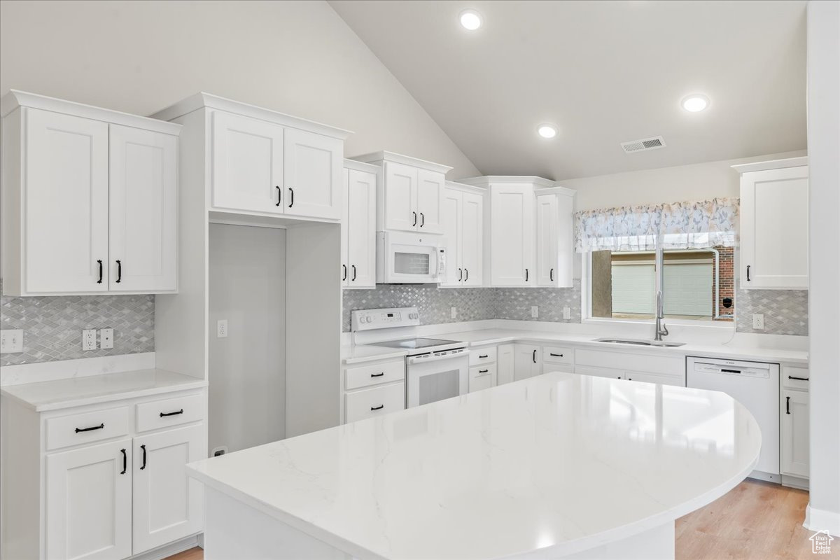 Kitchen featuring white cabinetry, sink, white appliances, and lofted ceiling