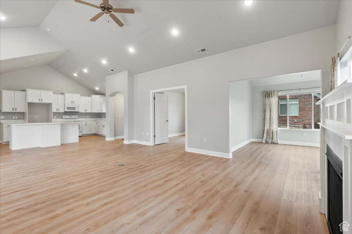 Unfurnished living room featuring high vaulted ceiling, ceiling fan, and light wood-type flooring