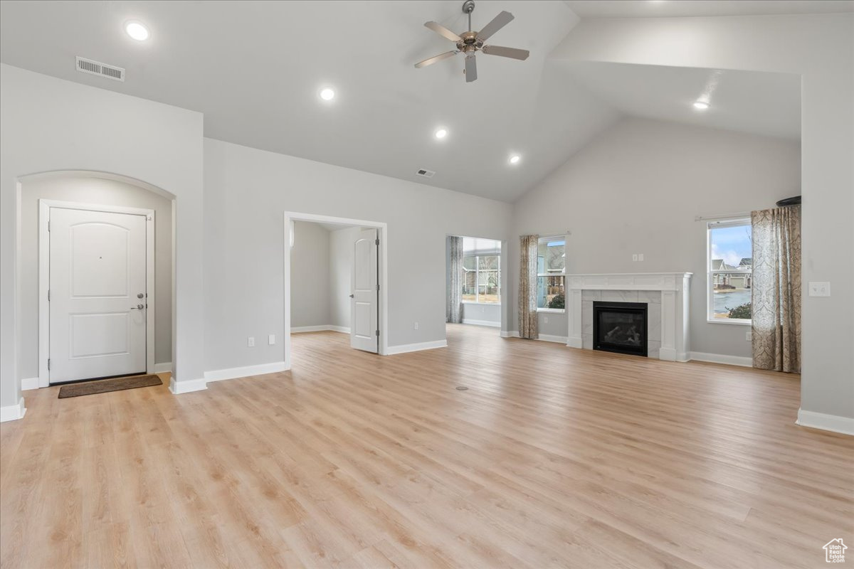 Unfurnished living room featuring ceiling fan, high vaulted ceiling, and light wood-type flooring