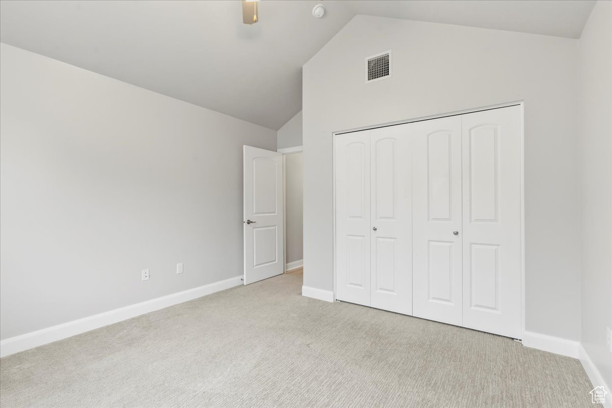 Unfurnished bedroom featuring ceiling fan, light colored carpet, high vaulted ceiling, and a closet