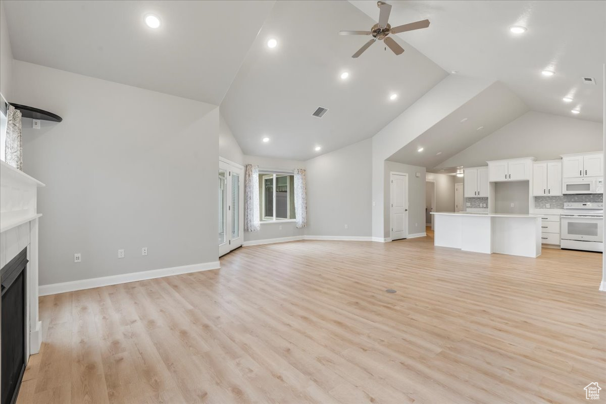 Unfurnished living room featuring ceiling fan, high vaulted ceiling, and light hardwood / wood-style flooring