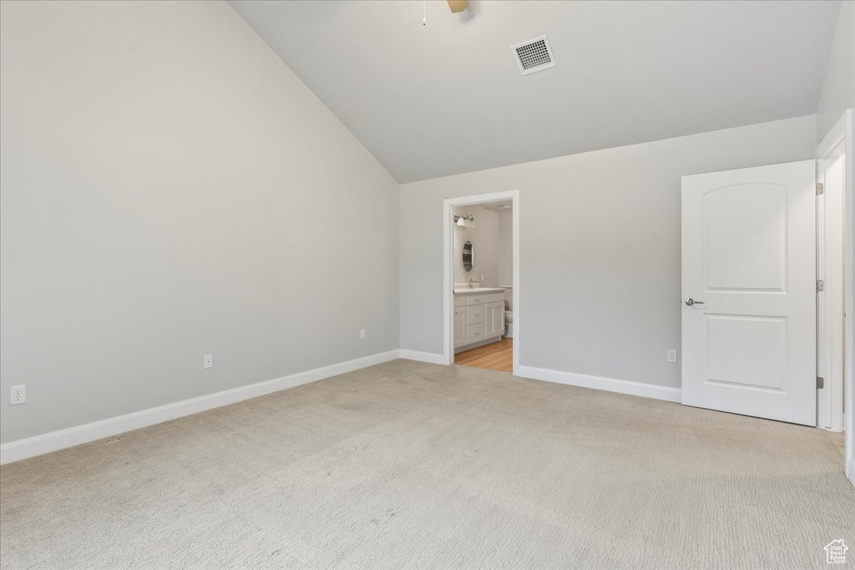 Unfurnished bedroom with light carpet, connected bathroom, and vaulted ceiling