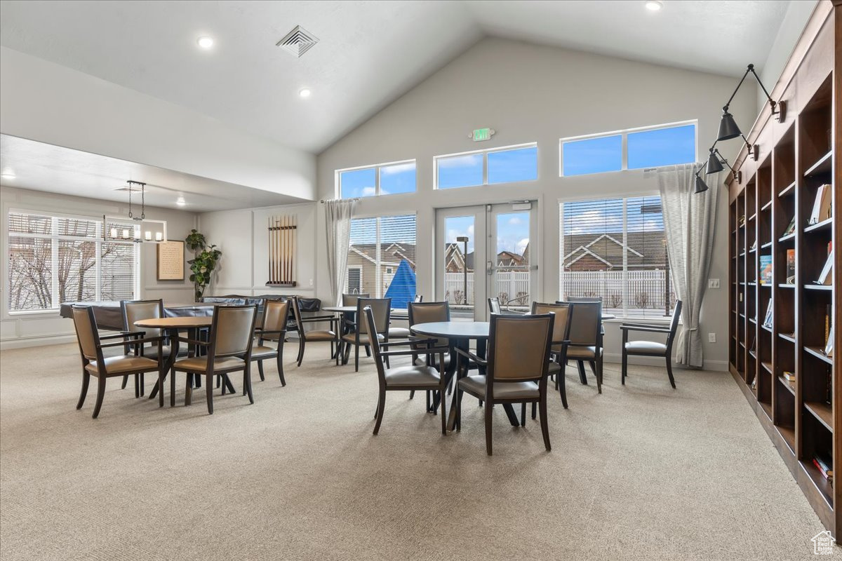 Dining area featuring french doors, light colored carpet, a chandelier, and high vaulted ceiling