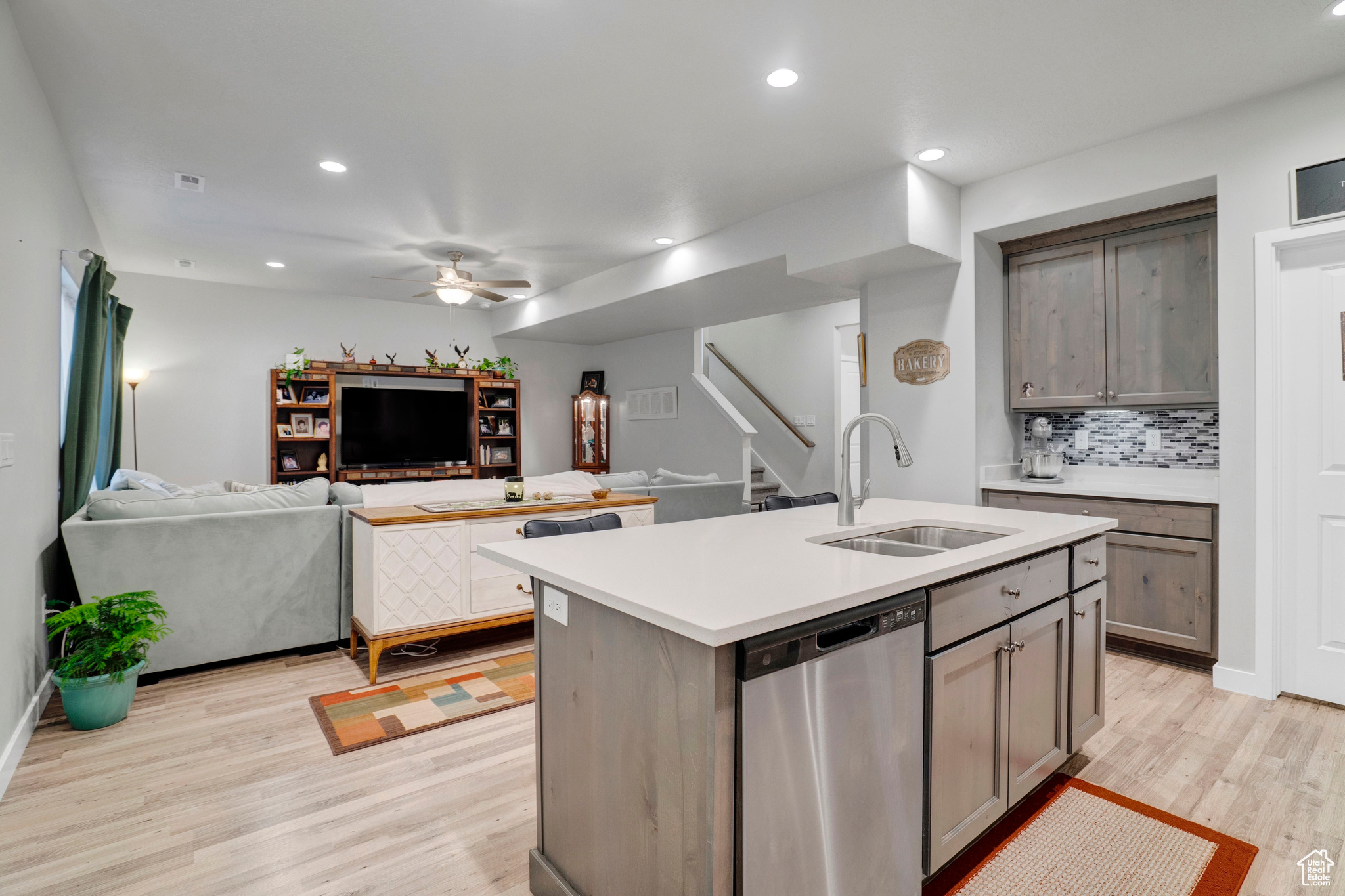 Kitchen with sink, dishwasher, tasteful backsplash, an island with sink, and light wood-type flooring