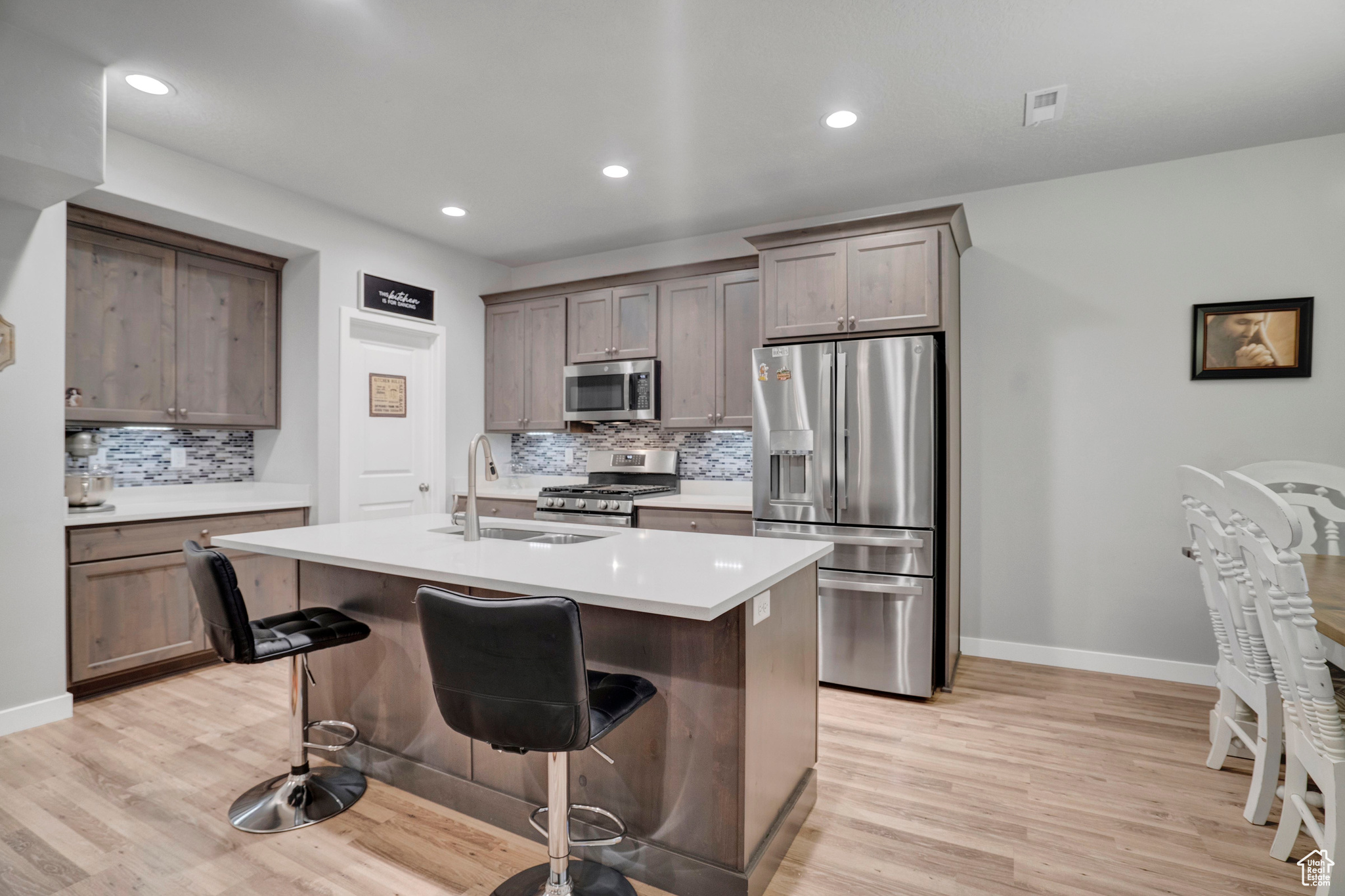 Kitchen featuring a kitchen bar, sink, light wood-type flooring, appliances with stainless steel finishes, and a kitchen island with sink