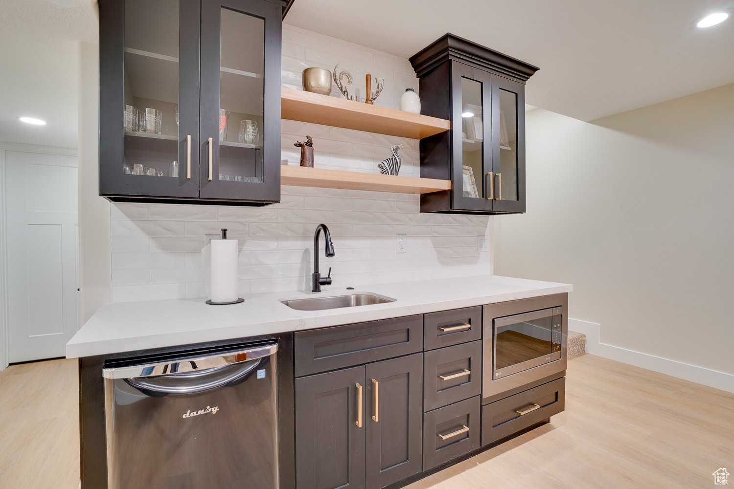 Bar featuring tasteful backsplash, appliances with stainless steel finishes, sink, and light wood-type flooring