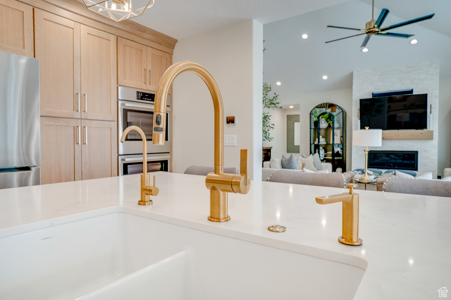 Kitchen featuring vaulted ceiling, appliances with stainless steel finishes, light brown cabinetry, a large fireplace, and ceiling fan