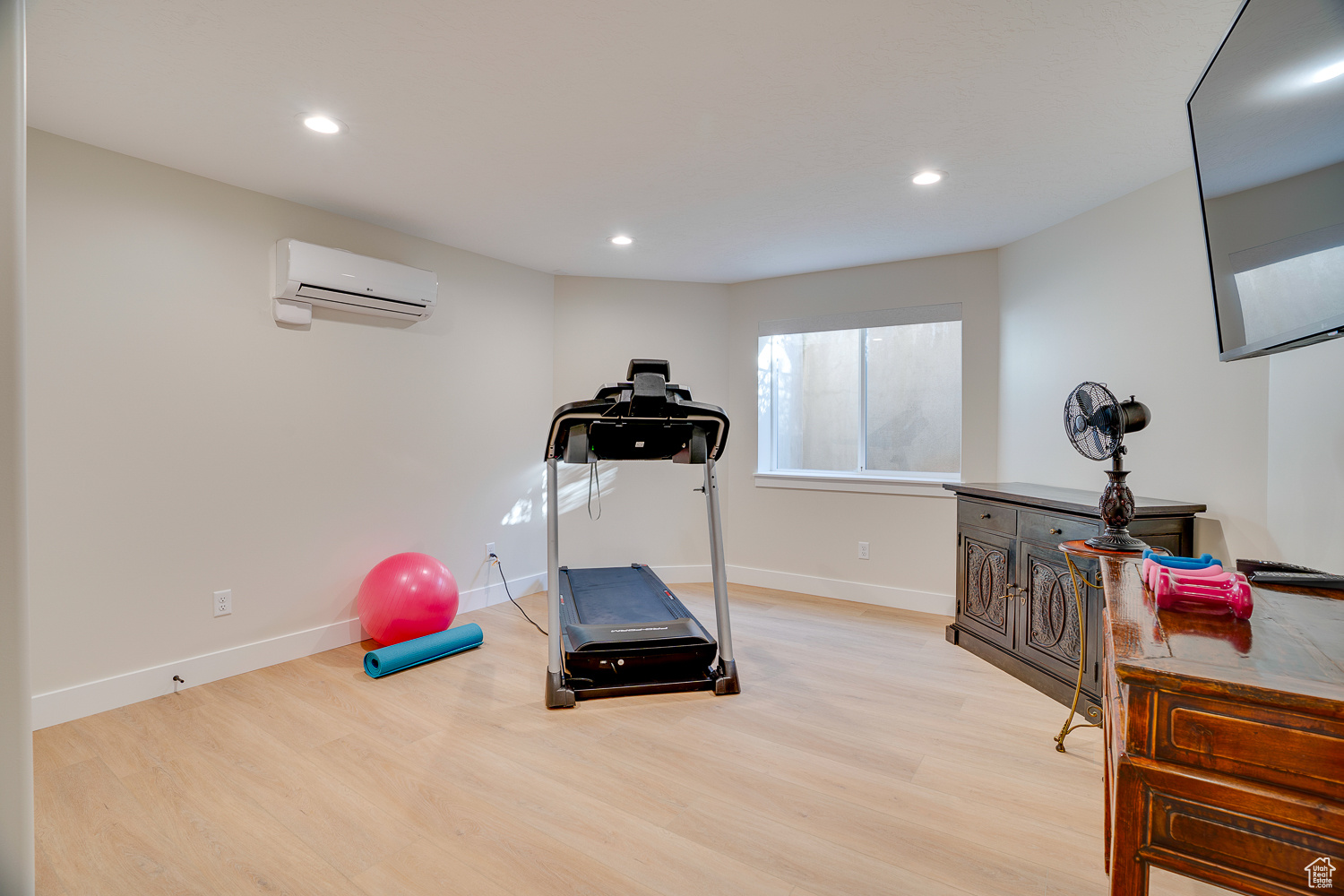 Workout room with a wall mounted AC and light wood-type flooring