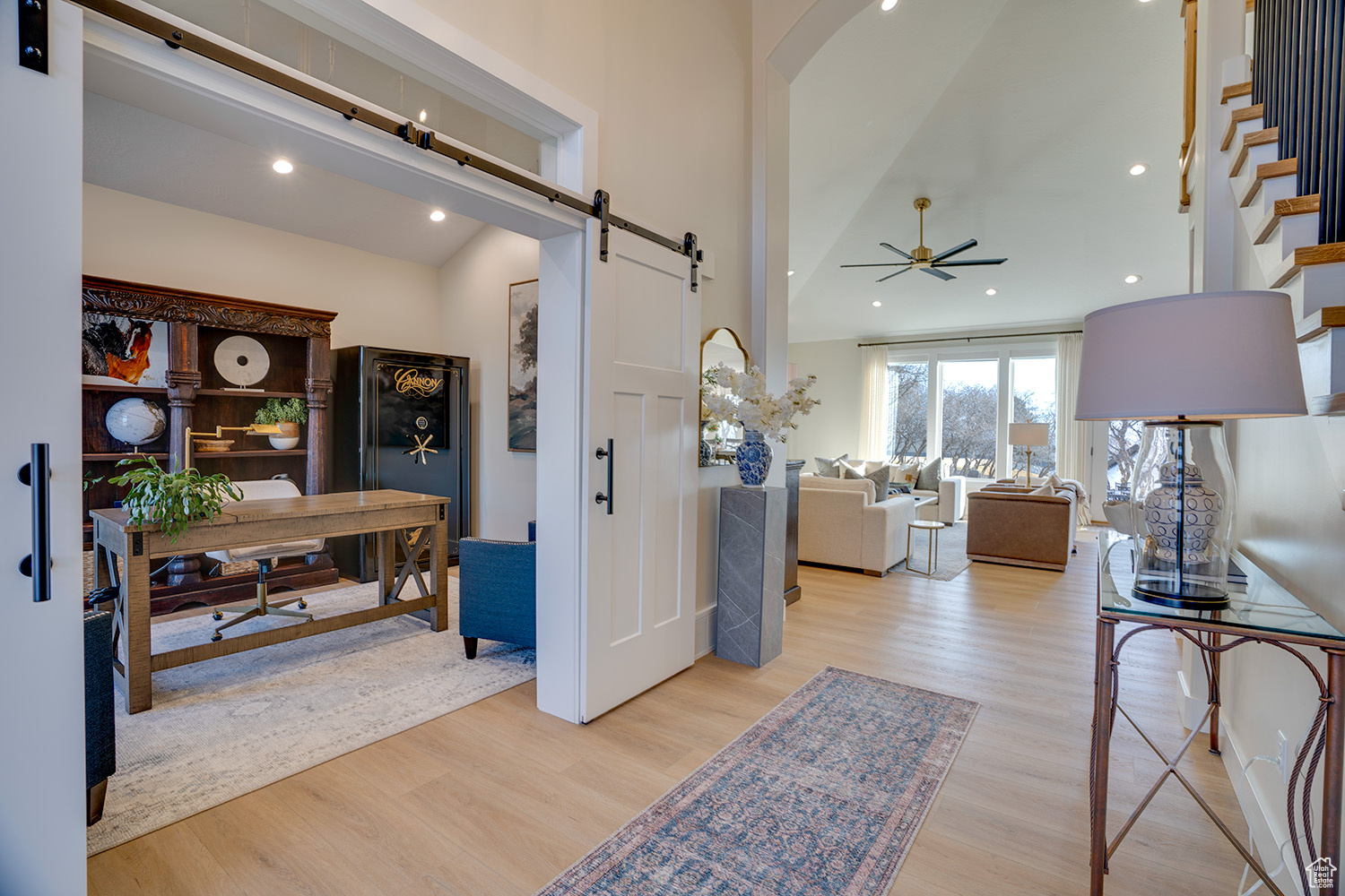 Living room featuring a high ceiling, a barn door, ceiling fan, and light wood-type flooring