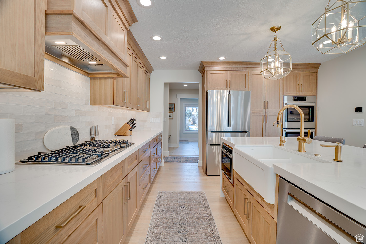 Kitchen with sink, light brown cabinets, appliances with stainless steel finishes, custom range hood, and pendant lighting