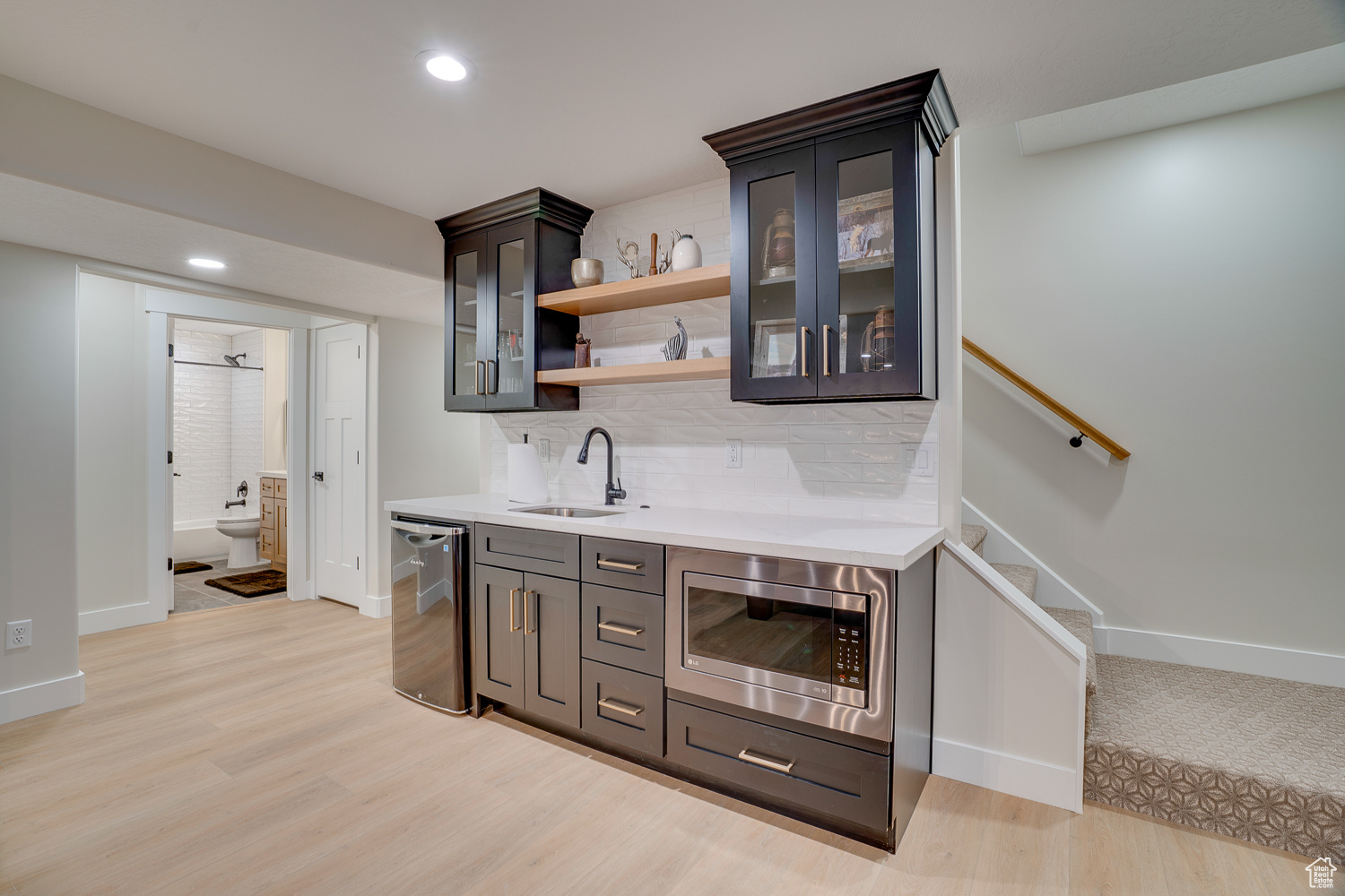 Bar featuring appliances with stainless steel finishes, sink, light hardwood / wood-style flooring, and backsplash