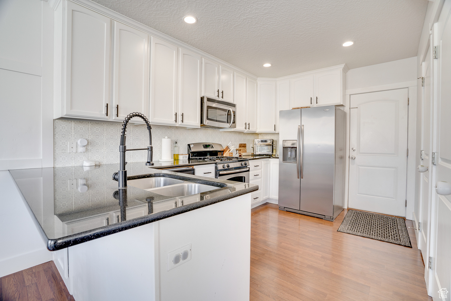 Kitchen featuring stainless steel appliances, white cabinets, and light hardwood / wood-style floors